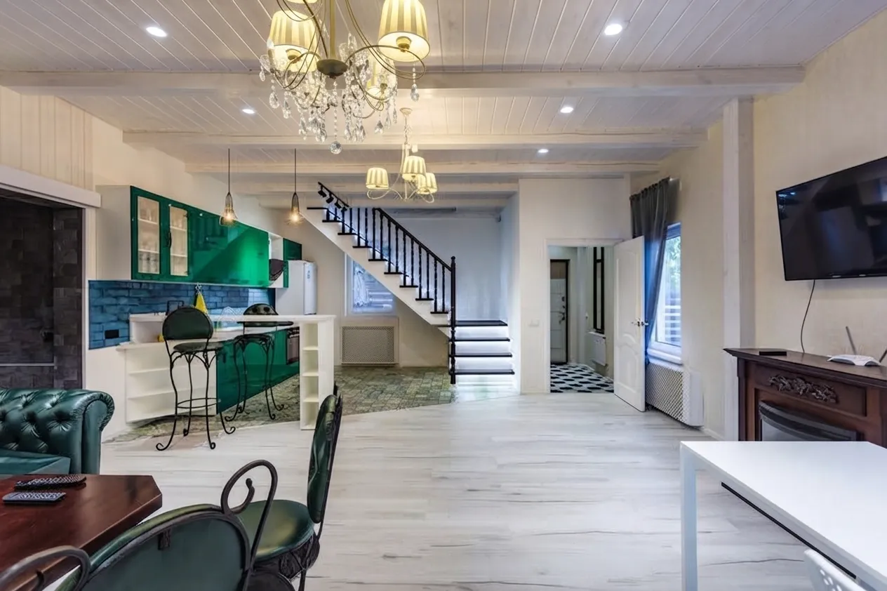 An open-plan living room with emerald green kitchen cabinets, a modern staircase, and dining area.