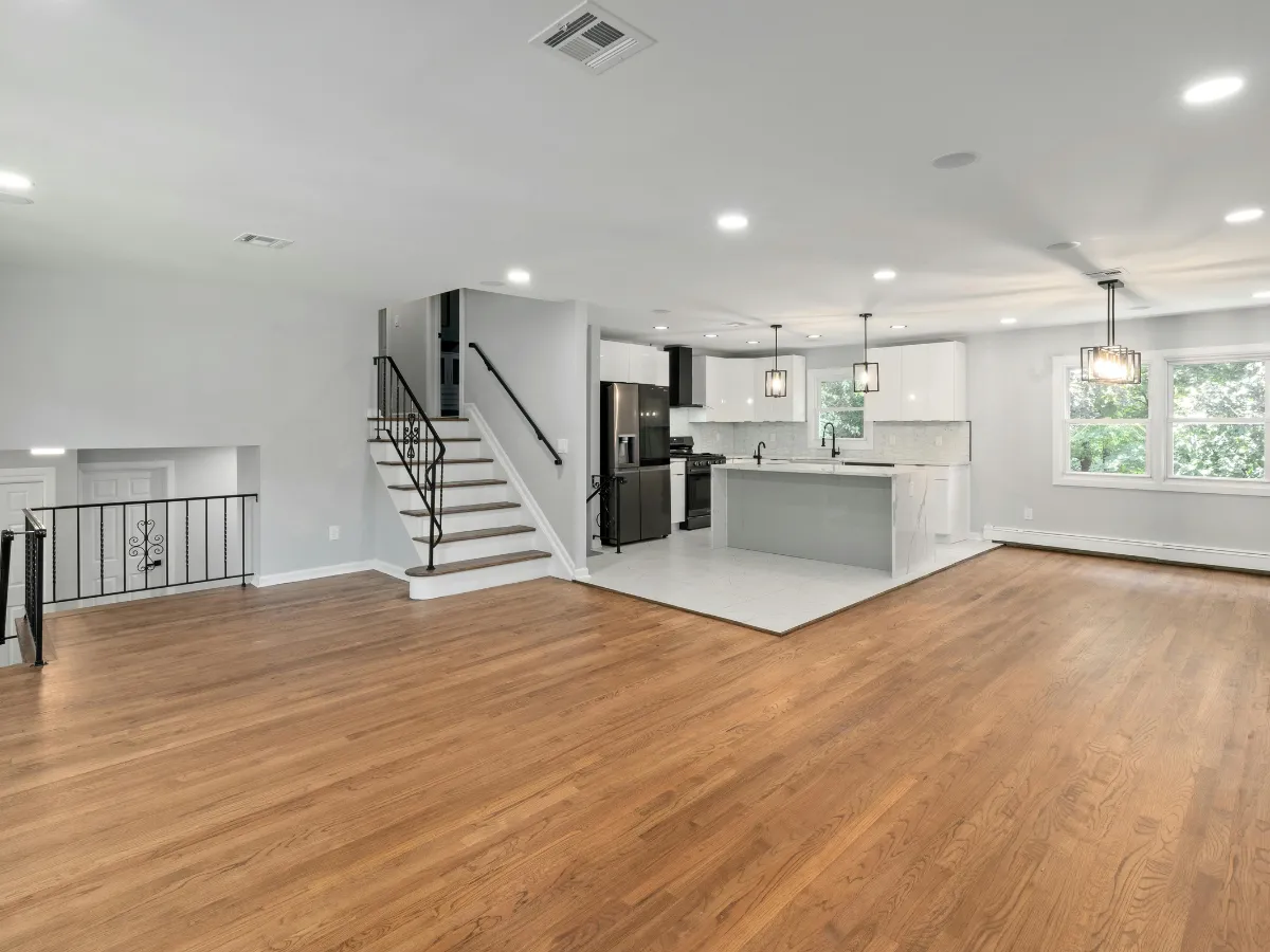 An open-concept interior features light hardwood floors, a black metal staircase, and a modern white kitchen with an island.