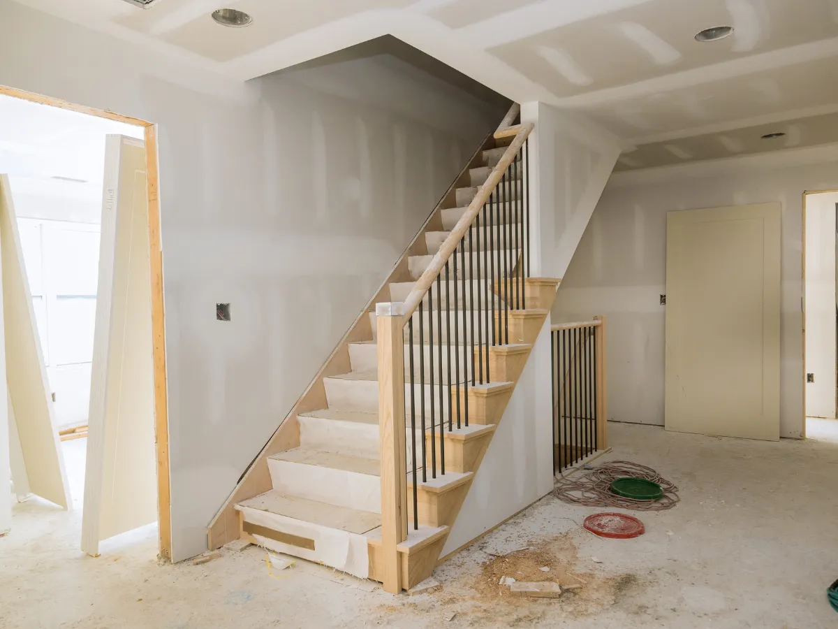 An unfinished new construction home interior showing a wooden staircase with black balusters and unpainted drywall.