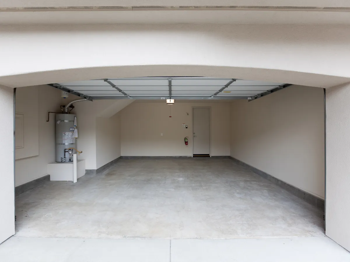 An empty, clean garage with an open door, a water heater in the corner, and an exit door visible inside.