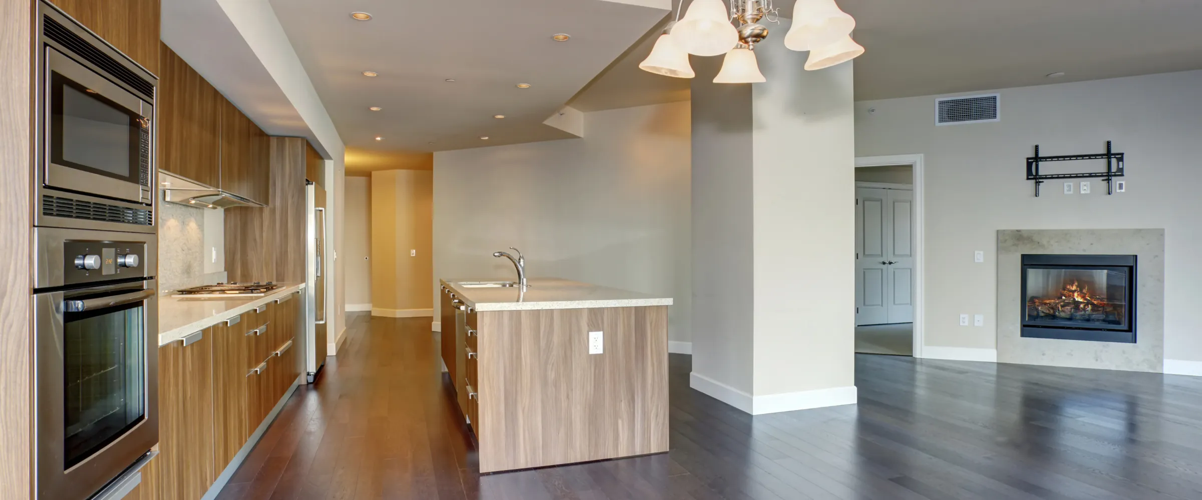 A modern open-concept kitchen and living room featuring a wood-paneled kitchen island, stainless steel appliances, dark hardwood floors, and a lit fireplace. A modern open-concept kitchen and living room featuring a wood-paneled kitchen island, stainless steel appliances, dark hardwood floors, and a lit fireplace.