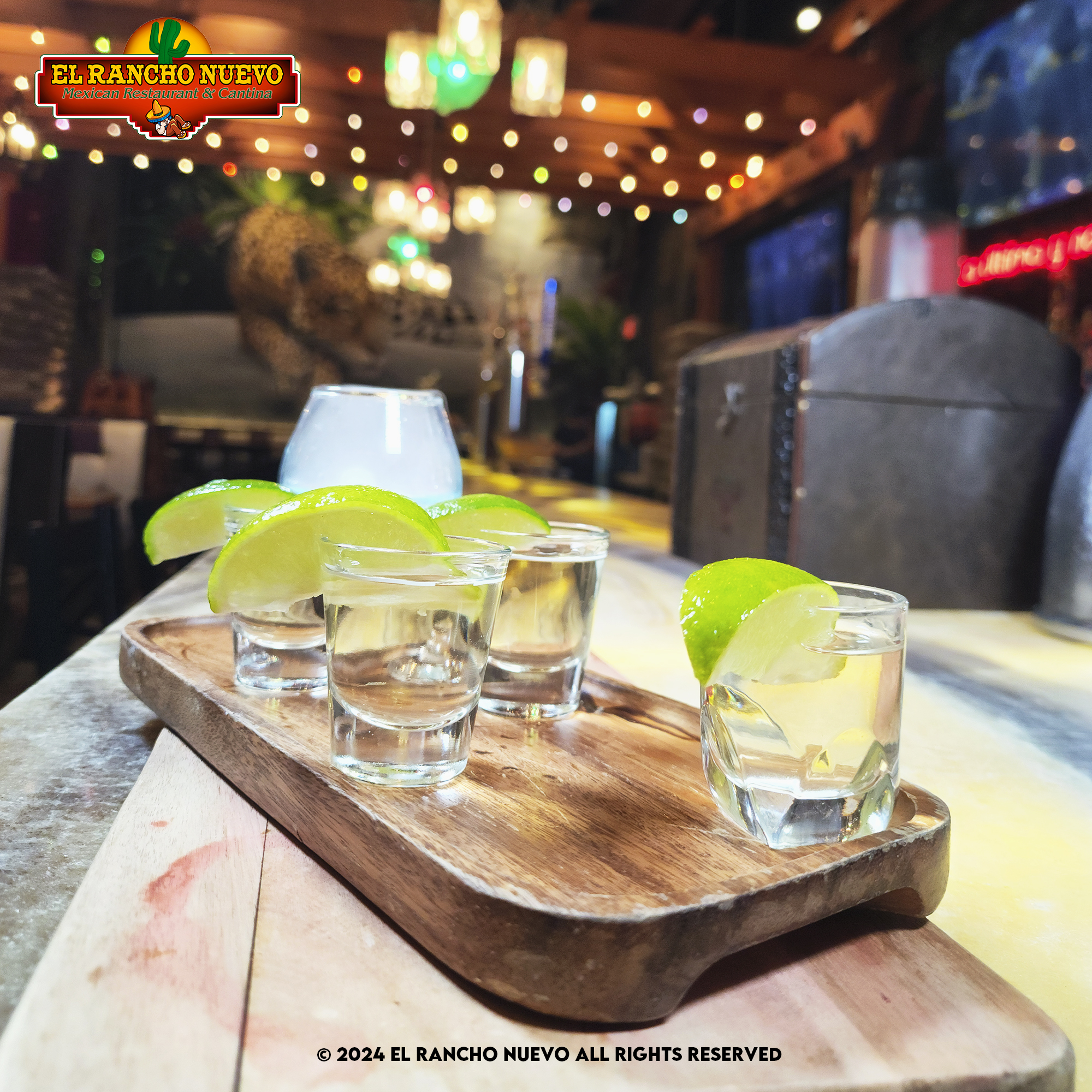 Four-glass tequila flight with lime on a wooden board beneath warm string lights