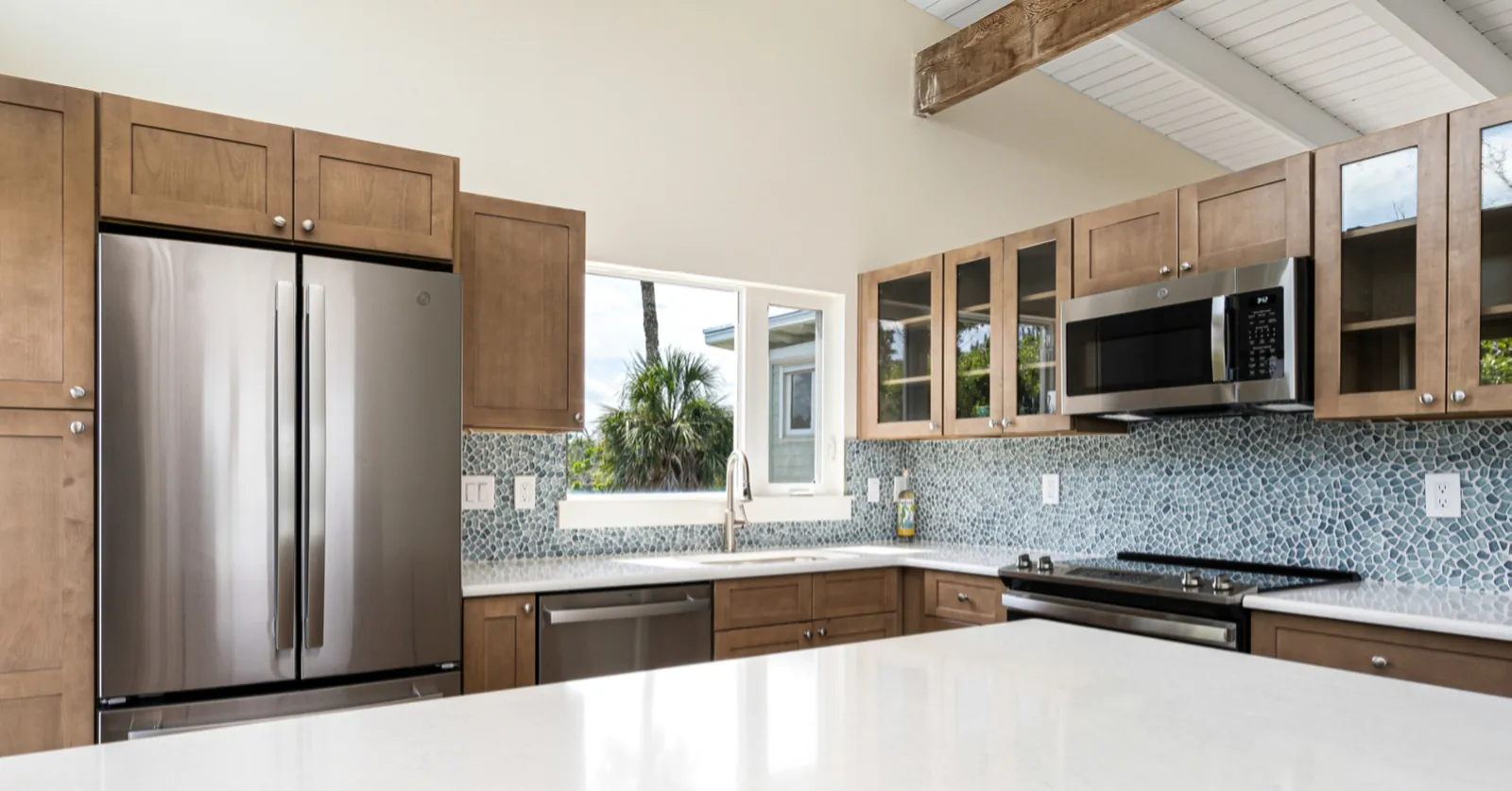 Kitchen with stained wood cabinets, glass-front uppers, blue mosaic tile backsplash, and white quartz island