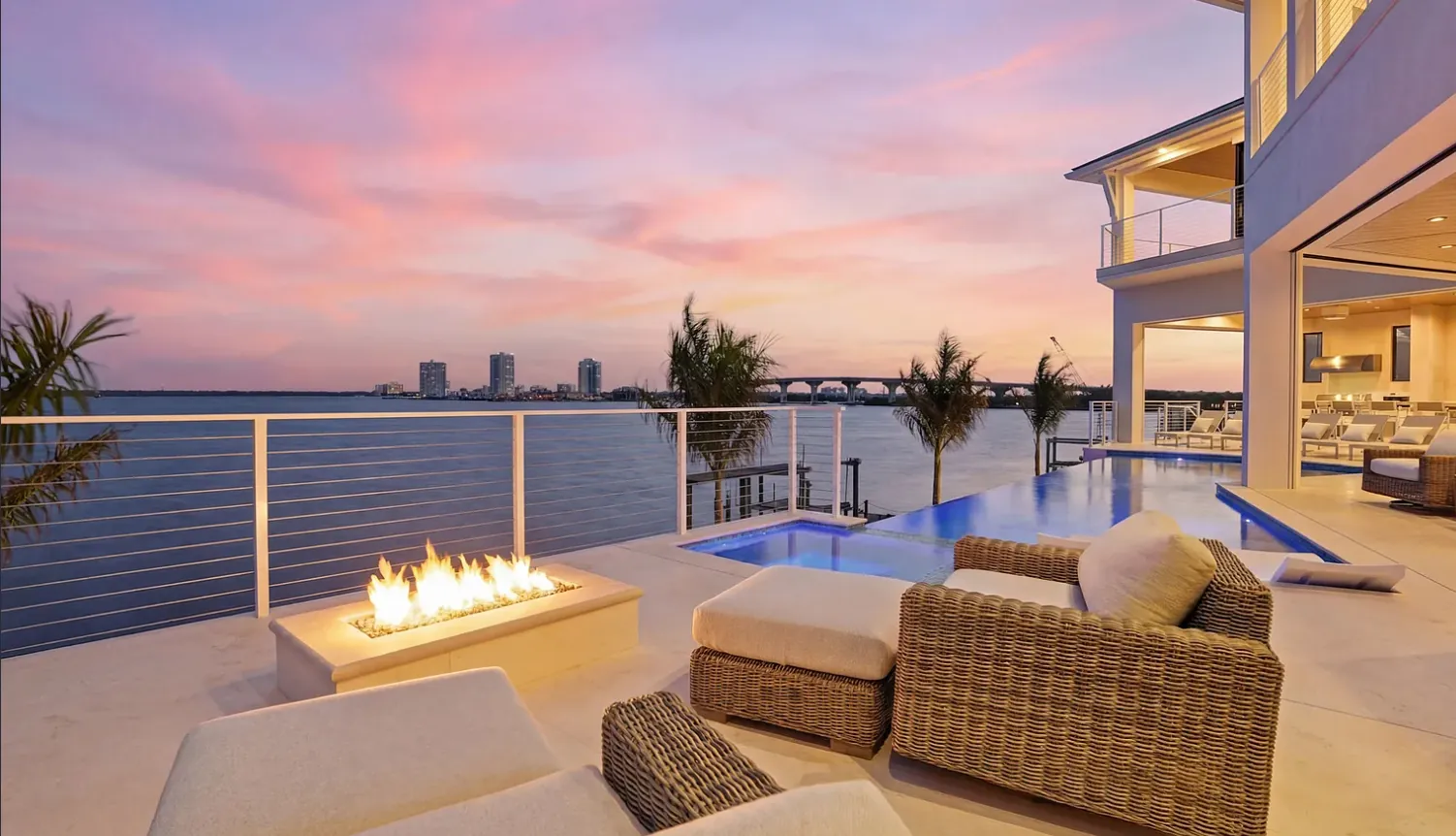 Waterfront pool deck with fire table and outdoor seating at sunset