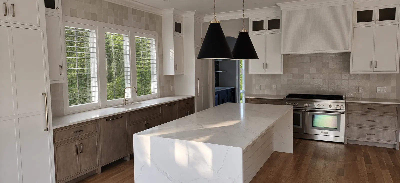 Kitchen with waterfall marble island, white and gray-stained custom cabinets, black pendants, and hardwood floors