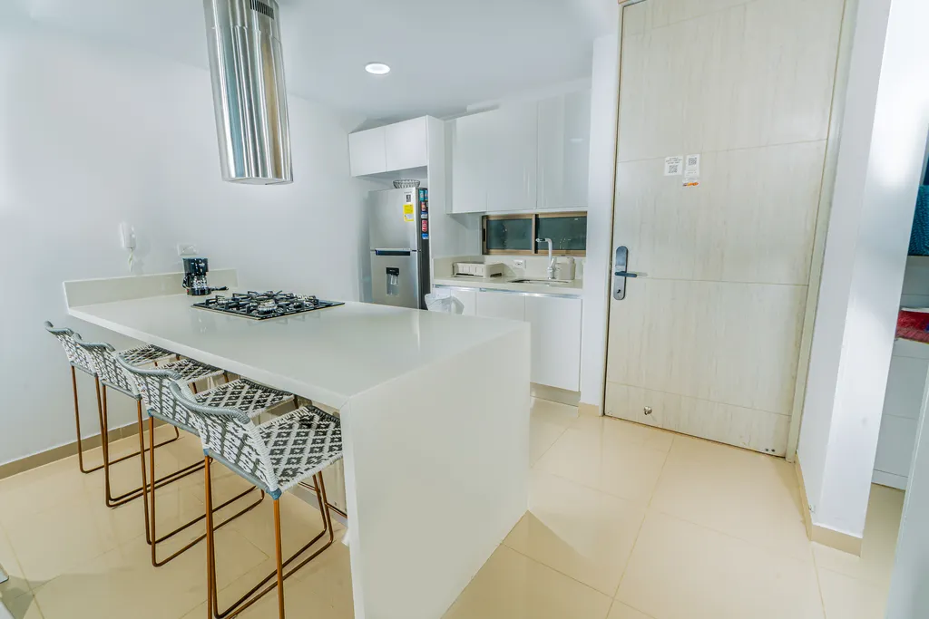 Cocina equipada con isla, taburetes, campana extractora y nevera de acero