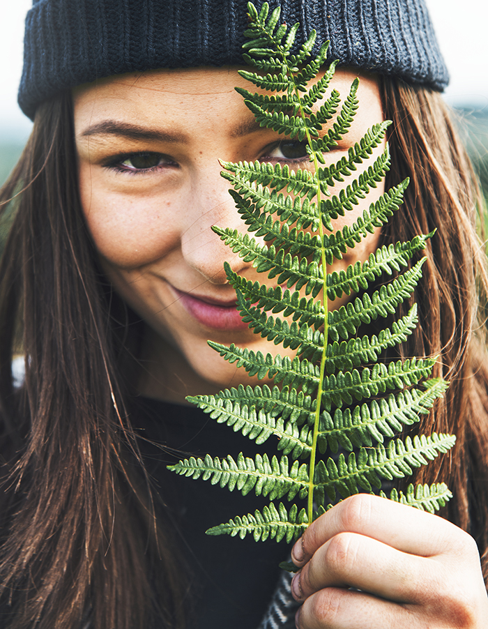 closeup photo of a woman's smiling face behind a fern leaf