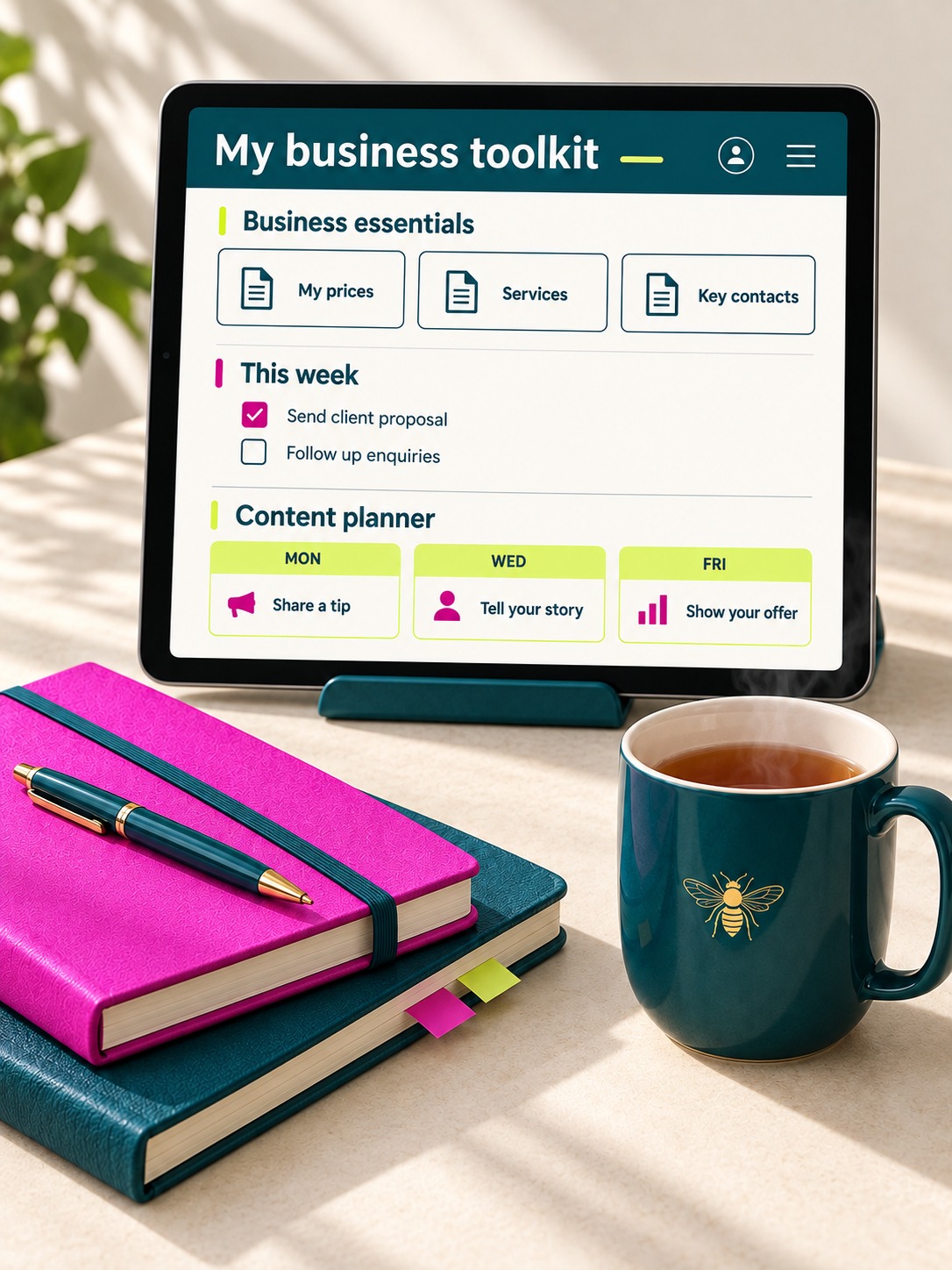 Desk scene with a tablet showing the My business toolkit dashboard, pink notebook and a teal bee mug