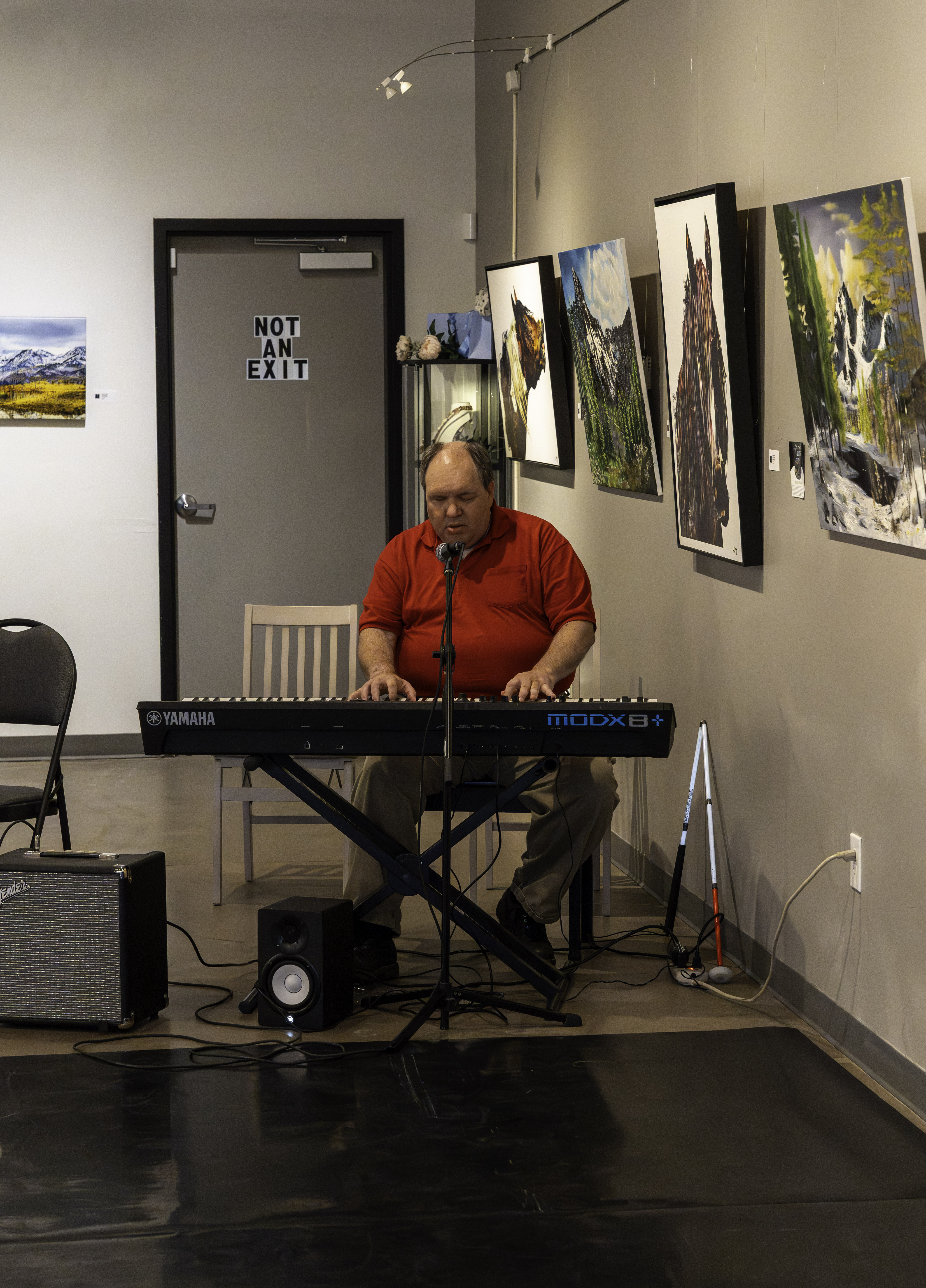 A blind musician performs on a keyboard during the Sight Unseen Showcase Performance at Create Gallery & Frames. A white cane rests beside him as he plays music surrounded by artwork on display. A blind musician performs on a keyboard during the Sight Unseen Showcase Performance at Create Gallery & Frames. A white cane rests beside him as he plays music surrounded by artwork on display.