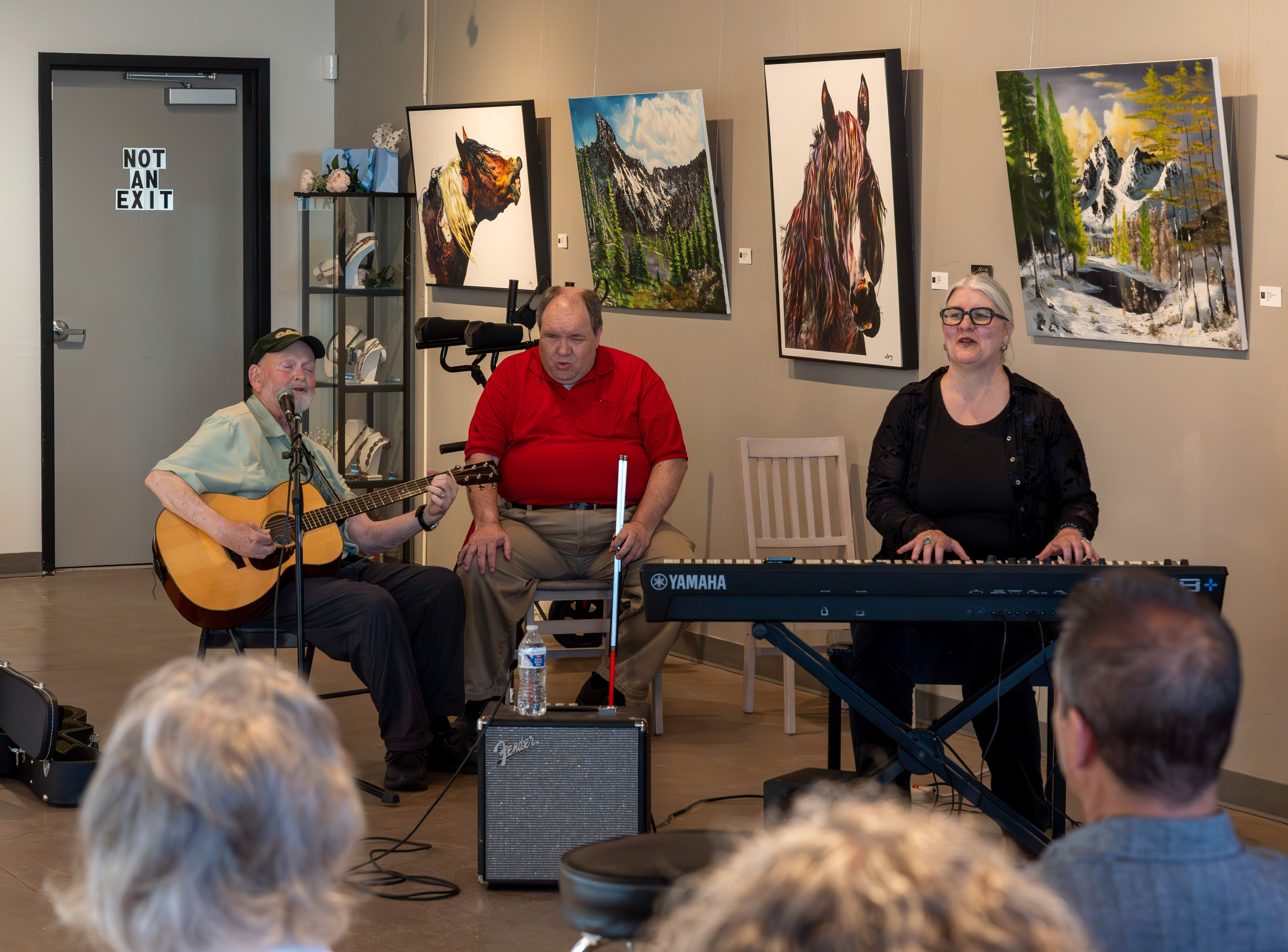 Three musicians perform during the Sight Unseen Showcase at Create Gallery & Frames. A blind guitarist sings while playing acoustic guitar, a blind pianist and vocalist performs beside him, and a sighted pianist accompanies the group as audience members listen and sing along. Three musicians perform during the Sight Unseen Showcase at Create Gallery & Frames. A blind guitarist sings while playing acoustic guitar, a blind pianist and vocalist performs beside him, and a sighted pianist accompanies the group as audience members listen and sing along.