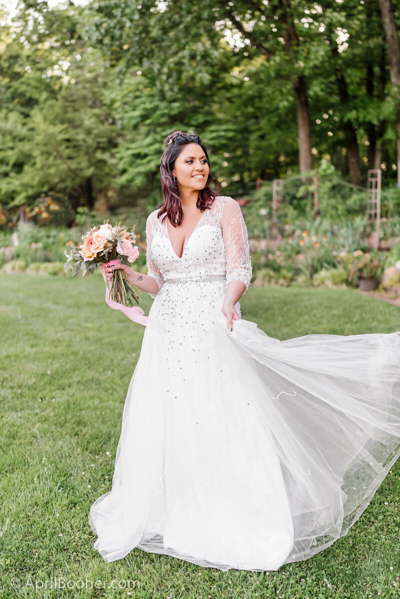 A bride smiles while walking in a garden lawn holding her train and looking over her shoulder captured by an East Tennessee wedding photographer.