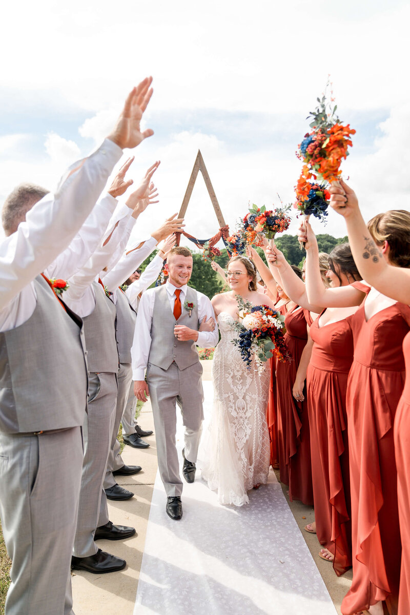 A bride and groom smile while walking arm in arm through a tunnel of their wedding party.