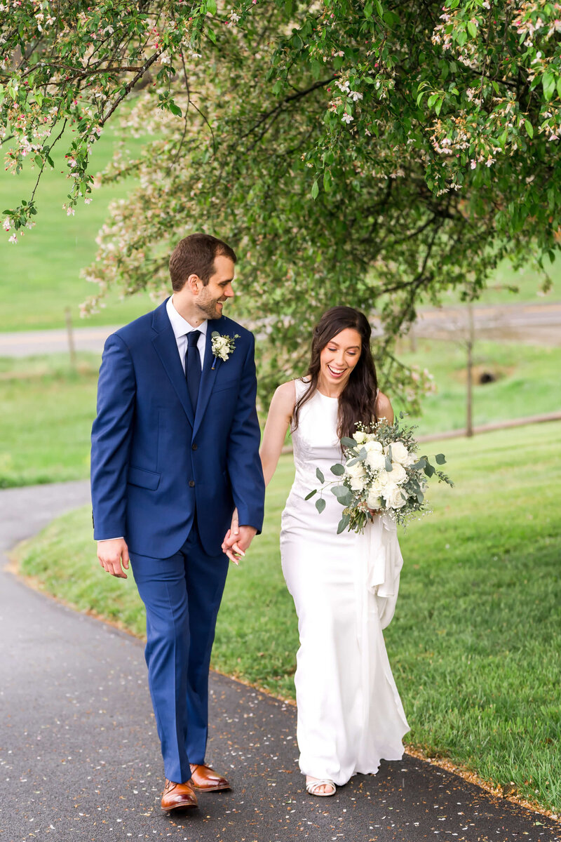 n image from a Johnson City wedding photography gallery of a bride smiling up to her tall groom in a blue suit under a blooming tree.