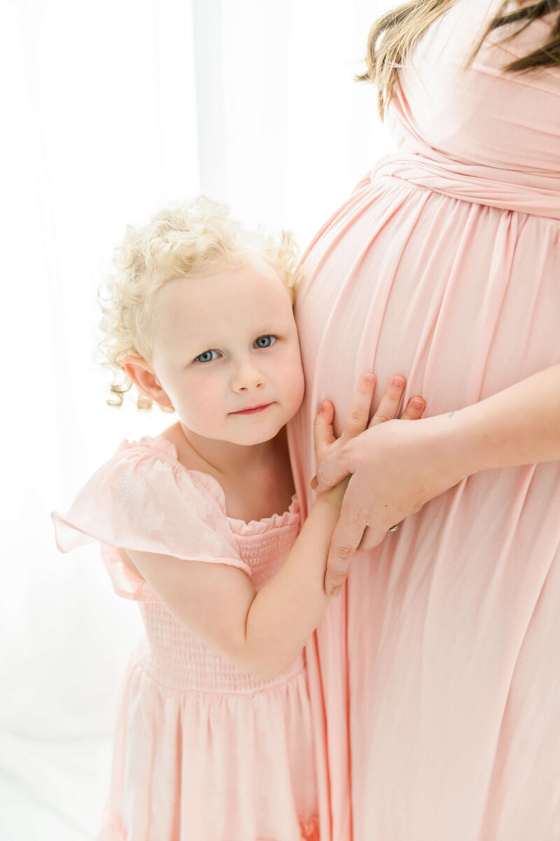A toddler girl listening to mom's pregnancy bump.