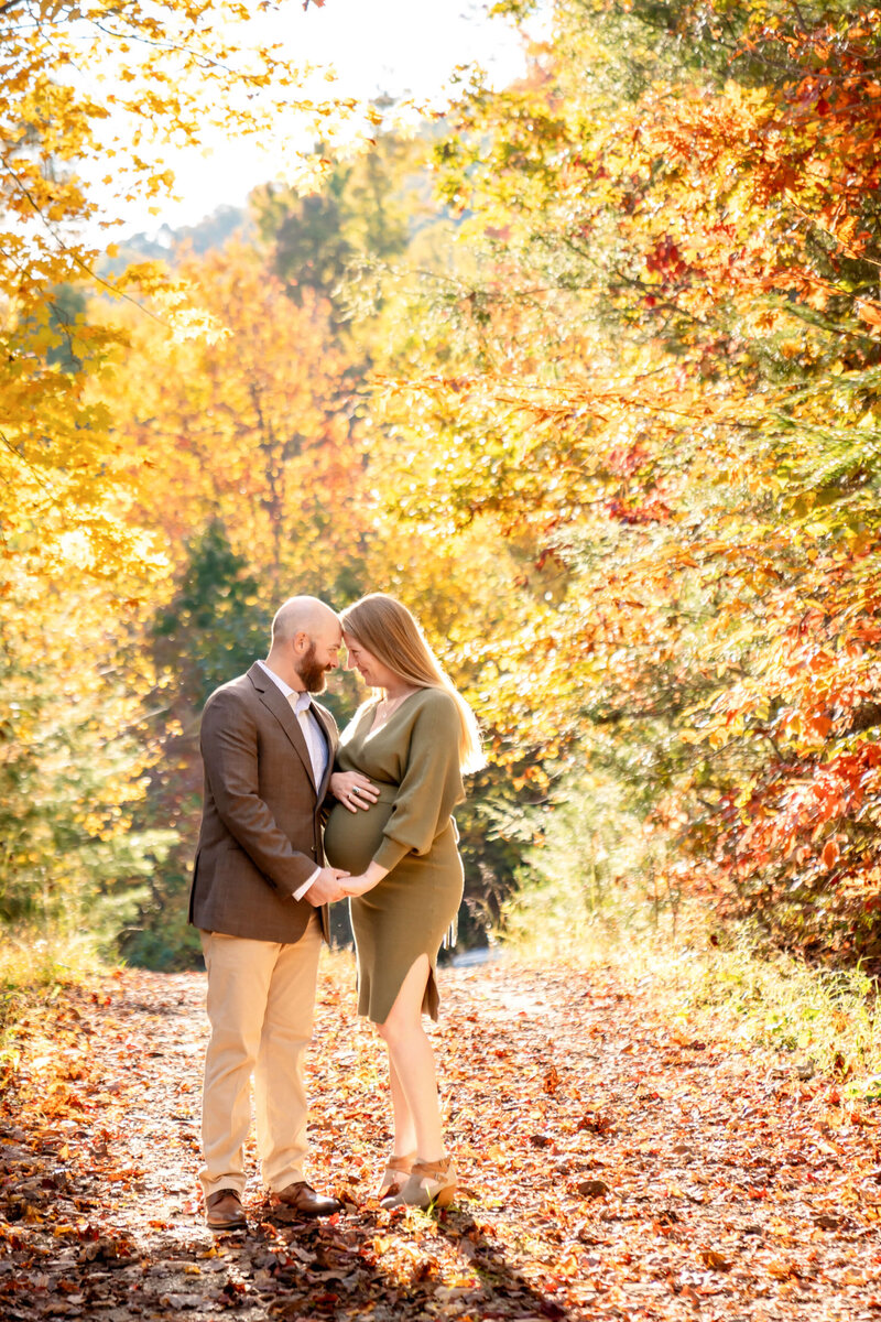 A mom to be in a grey flower print maternity dress touches foreheads and holds the bump with her husband in grey in a park sidewalk.