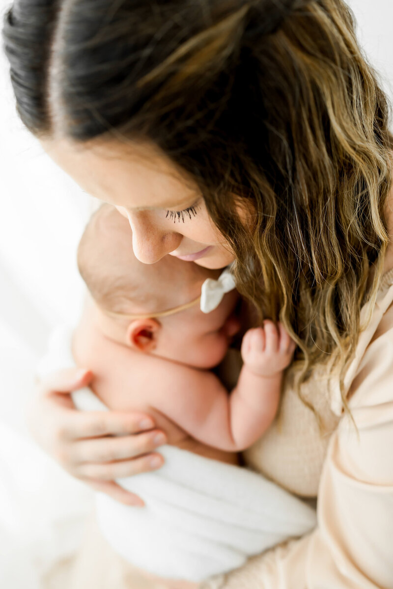 Mother cuddling her newborn baby girl close to her chest during a newborn session.