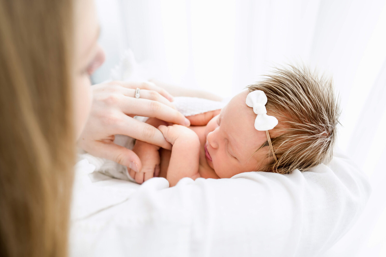 A sleeping newborn holds mom's finger while laying on a white bed.