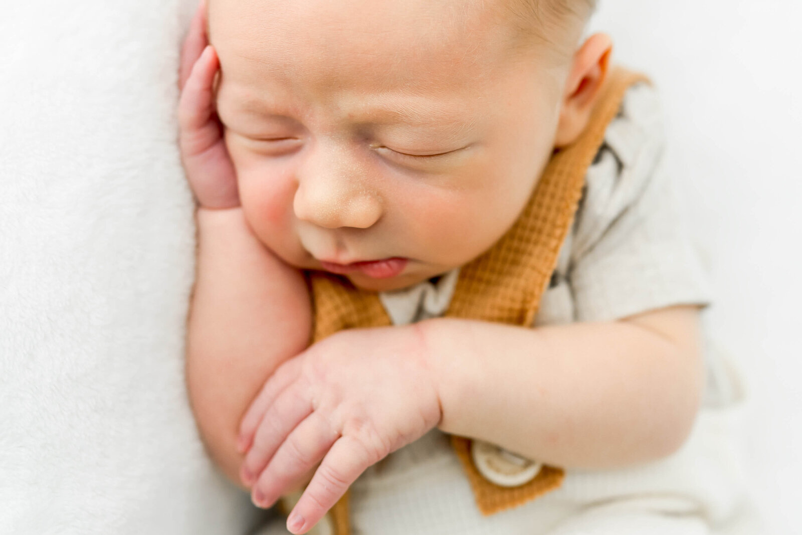 A closeup image of a newborn baby sleeping in orange overalls on his side.