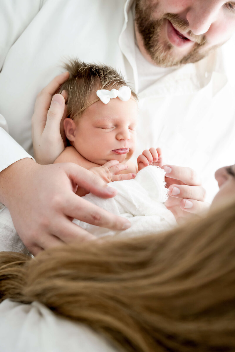 A newborn sleeps while supported by  mom dad.