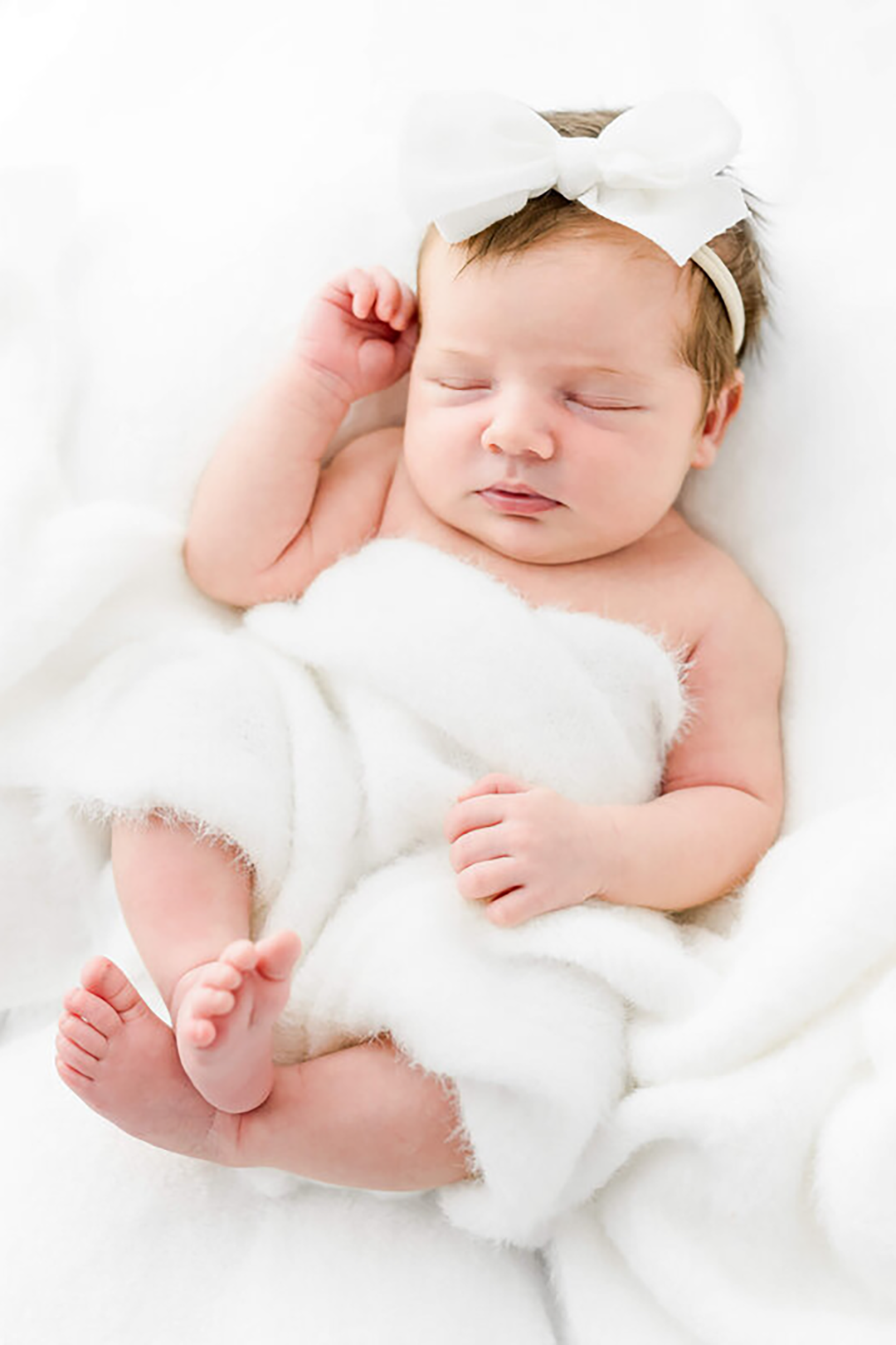 A baby sleeps under a cozy blanket on her back with a large headband.
