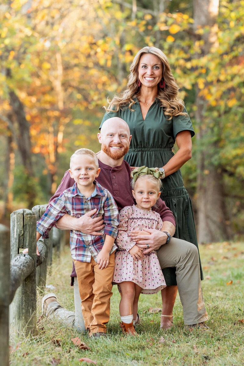 A mom in a green dress stands behind her kneeling husband with their two toddlers during a Johnson City family photography session.