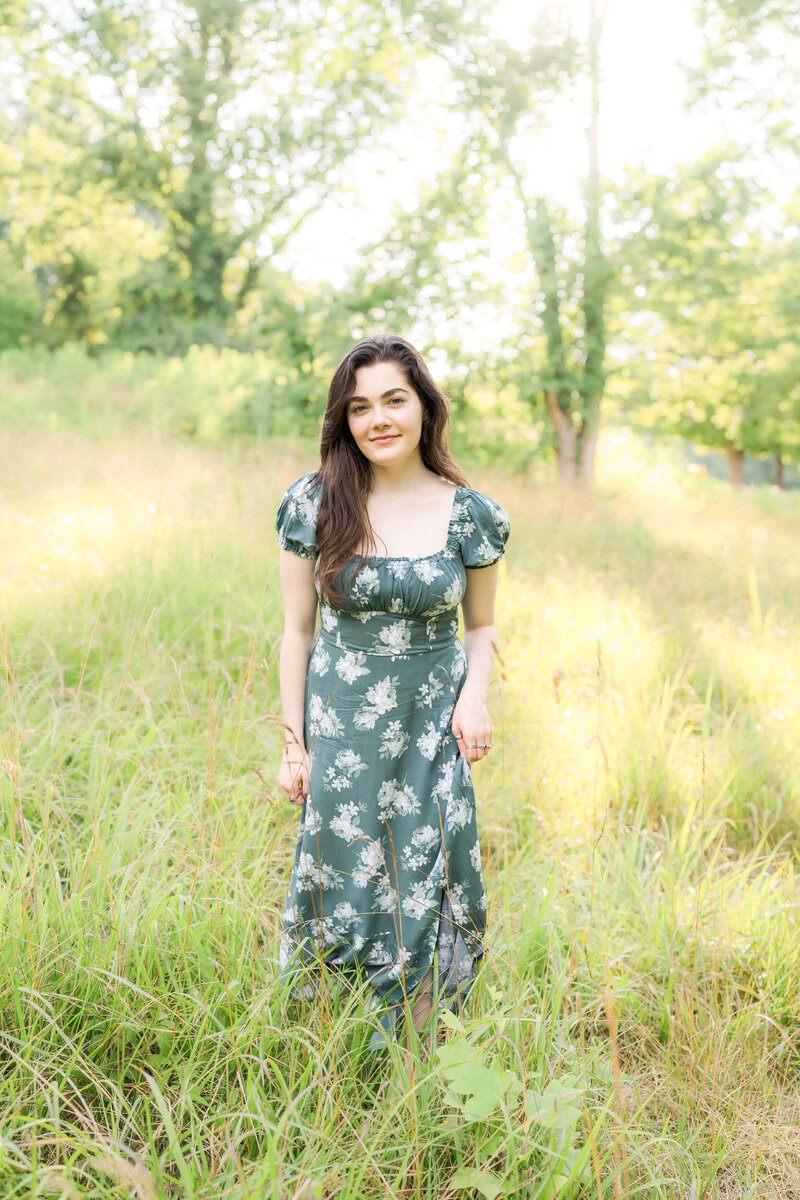 An expecting couple in green and brown snuggle holding hands under the bump in a park in the fall captured by their Johnson City maternity photographer.