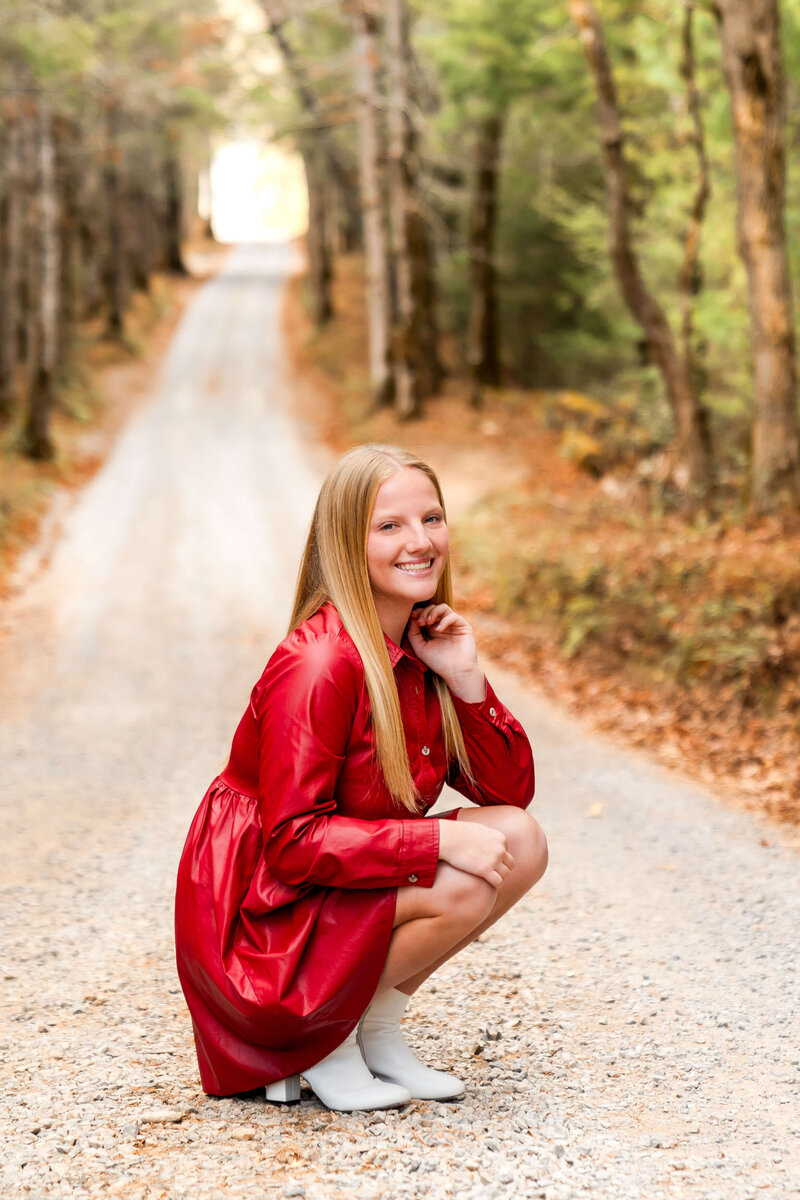 A woman kneels in a forest park trail at sunset in a red dress.