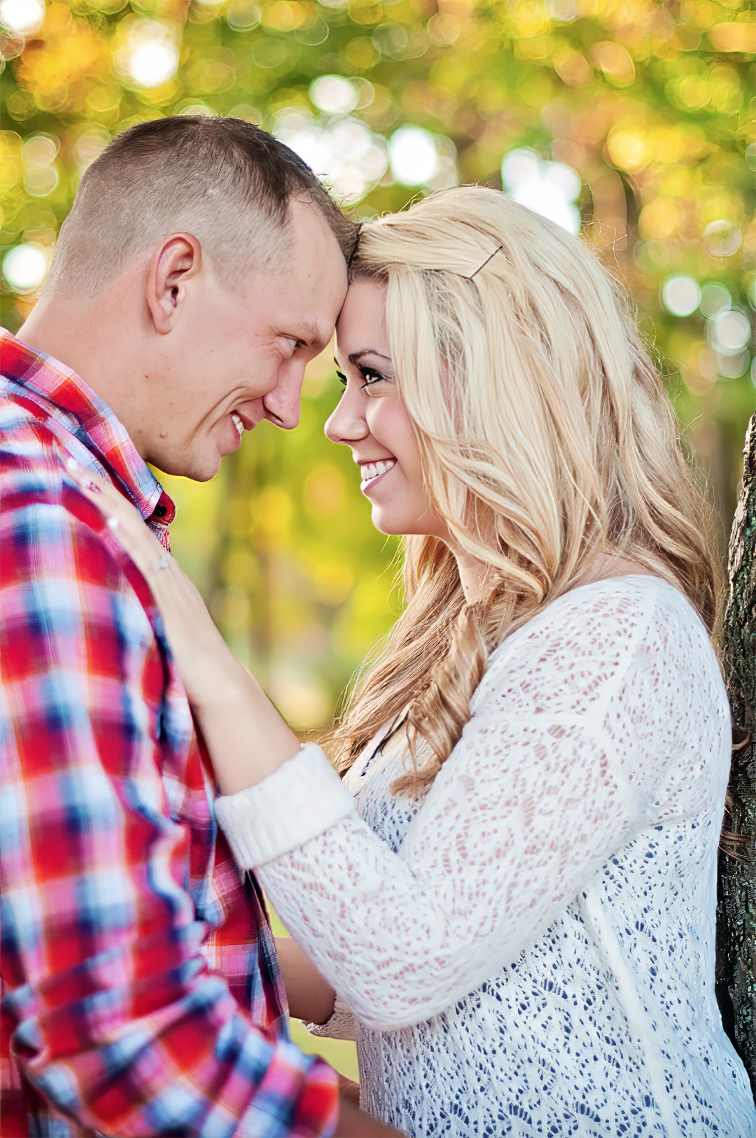 A couple stands with their foreheads touching while smiling at each other in an embrace.