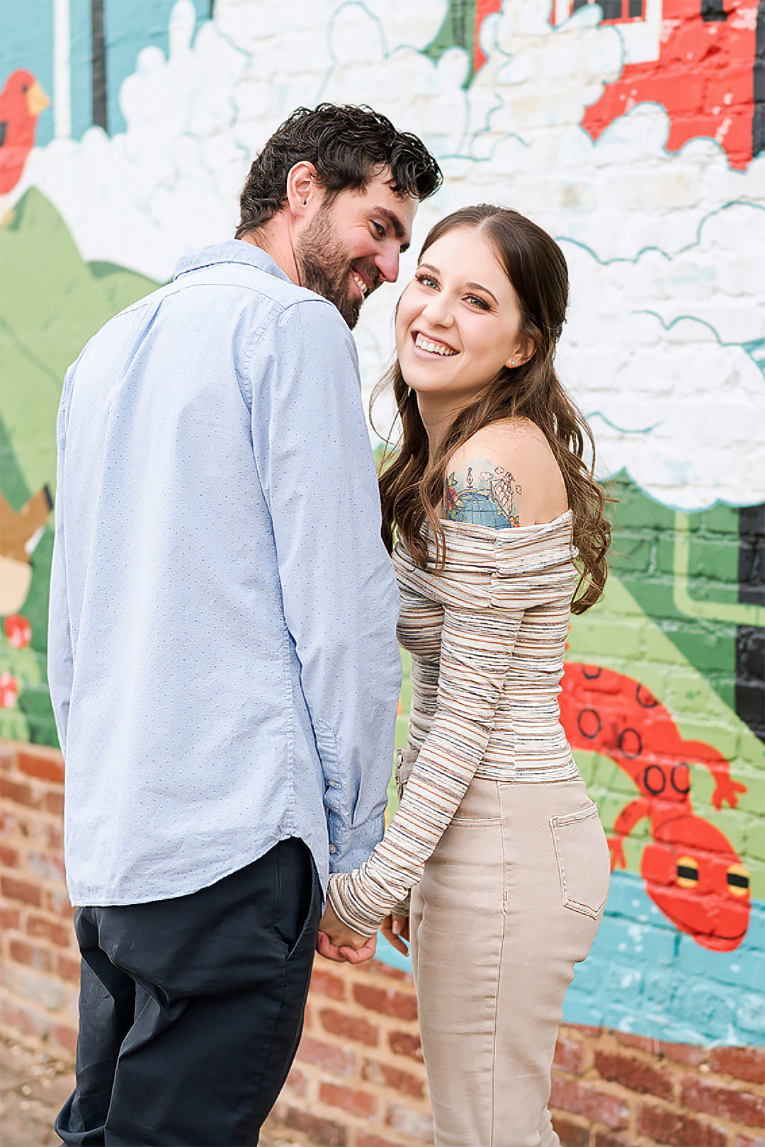 A happy bride smiles at her groom in a black tux while out in the sunset with veil flying around them.