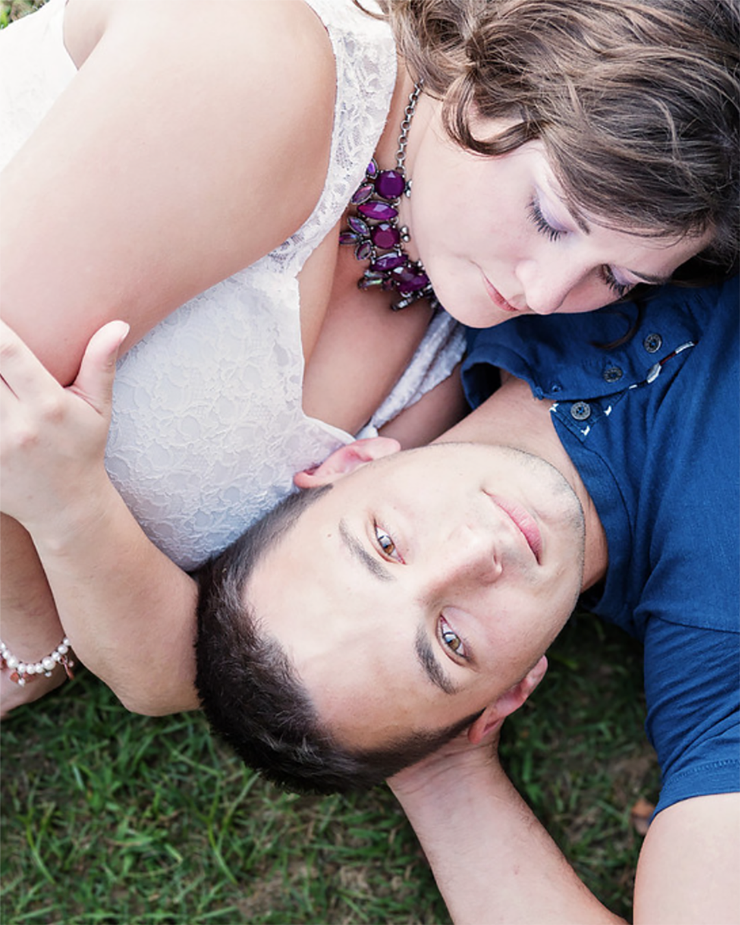 A couple layes in the grass cuddling during their engagement session.