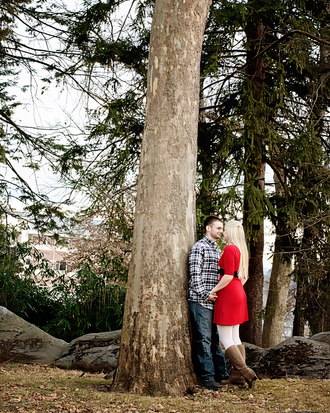A man leans on back on a tree while holding the hand of his partner in a grove of trees.