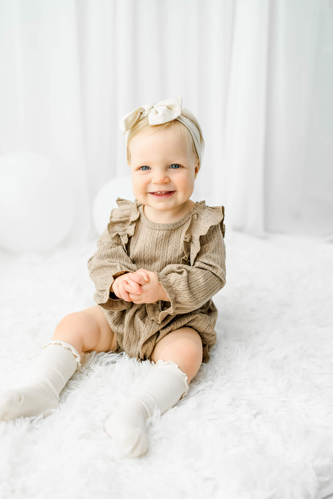 A new mom with dark hair snuggles her sleeping newborn cheek to cheek on a white bed.