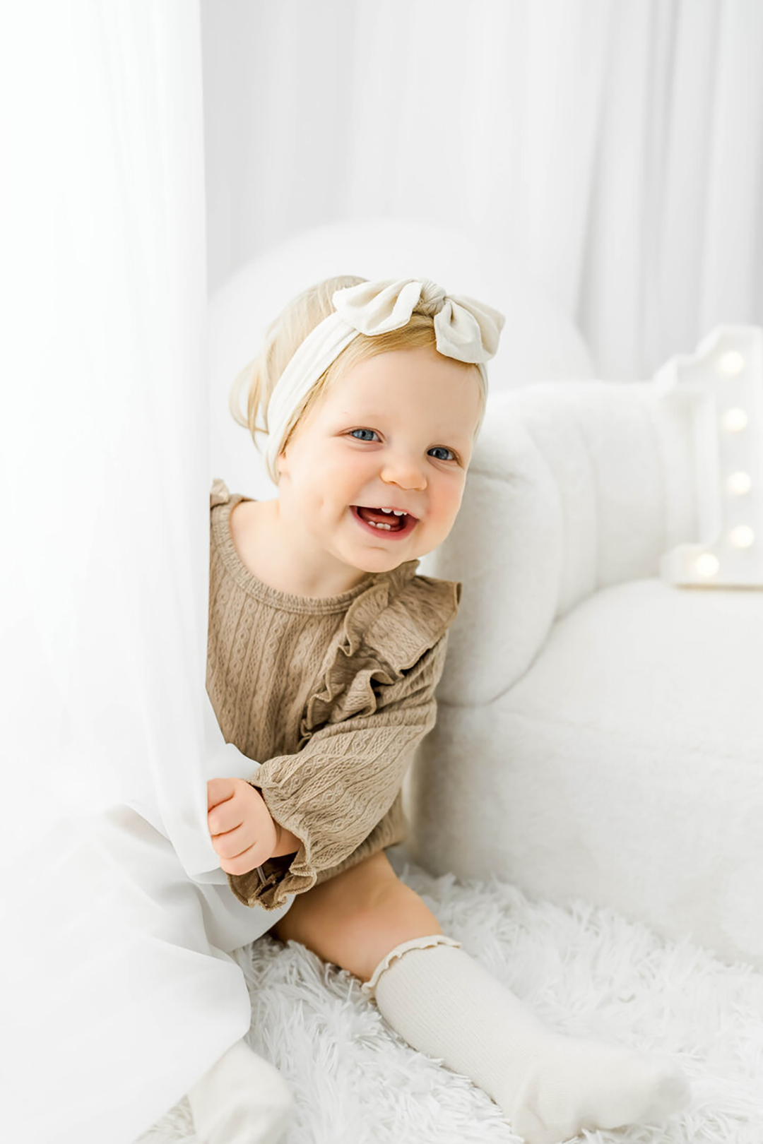 A newborn with a white bow sleeps against mom's chest in dad's hands as they snuggle.
