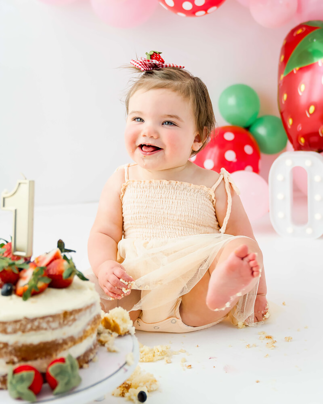 A cake smash birthday session with a little girl in yellow with strawberry cake and strawberry balloons.