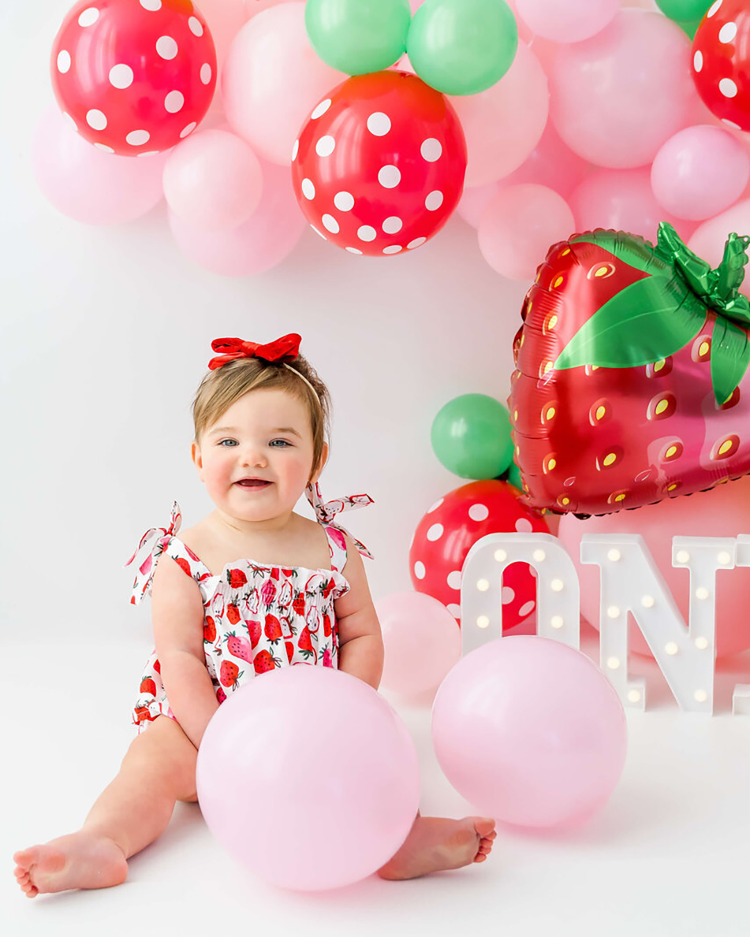 A little girl's first birthday in a strawberry dress with strawberry balloons.