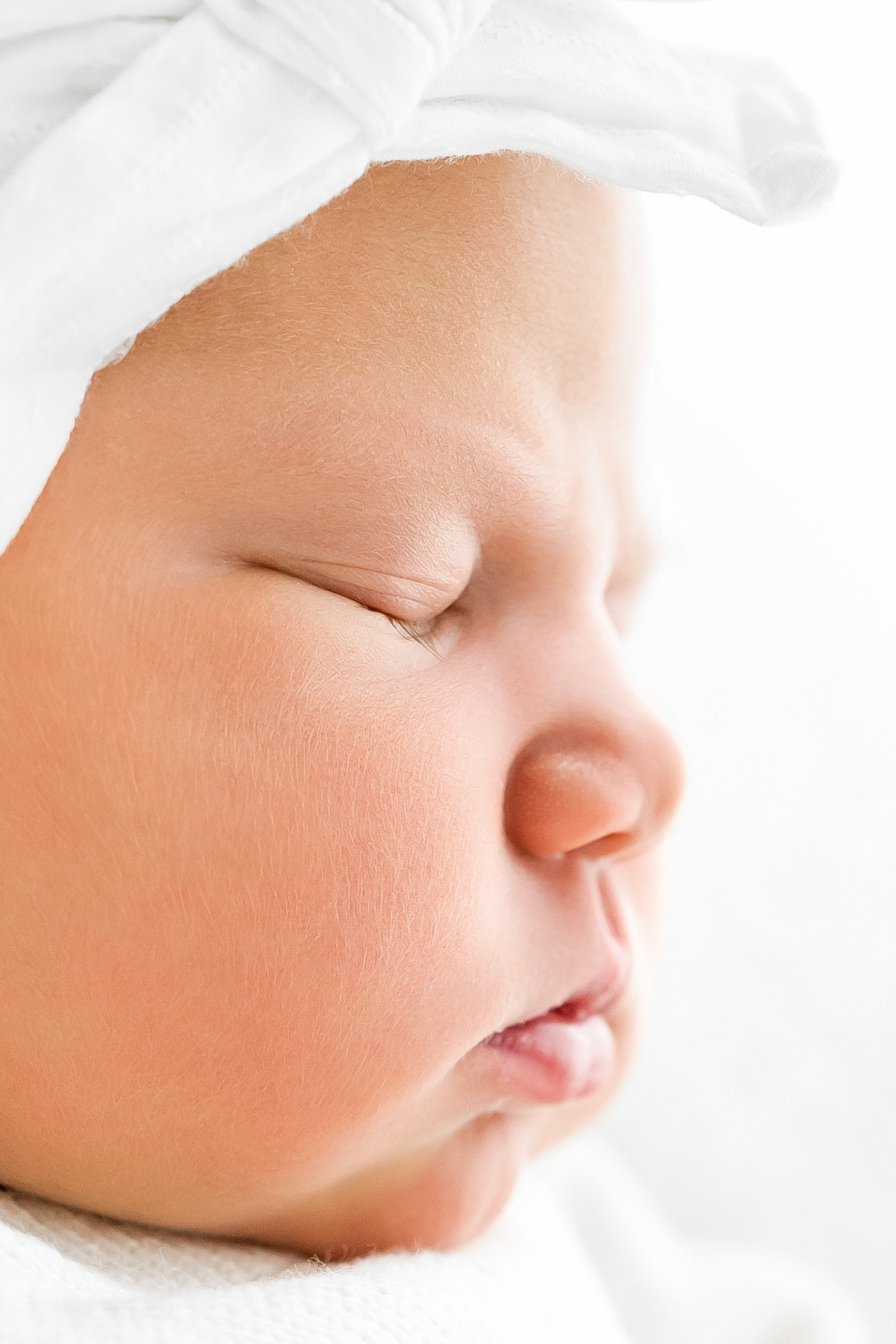 Close-up profile of a sleeping newborn baby wrapped in white.