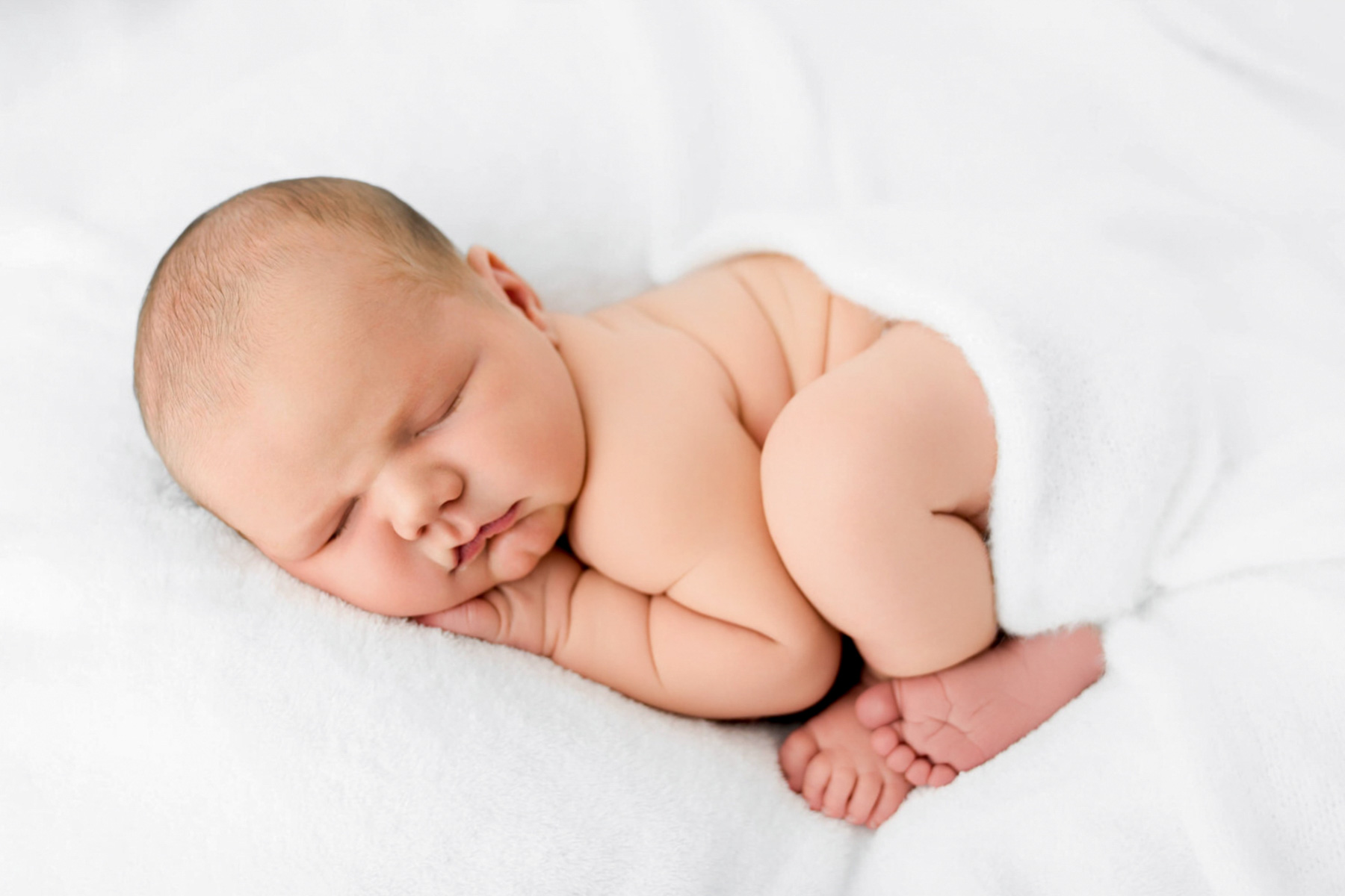 Sleeping newborn baby curled on a soft white blanket in a natural newborn portrait.