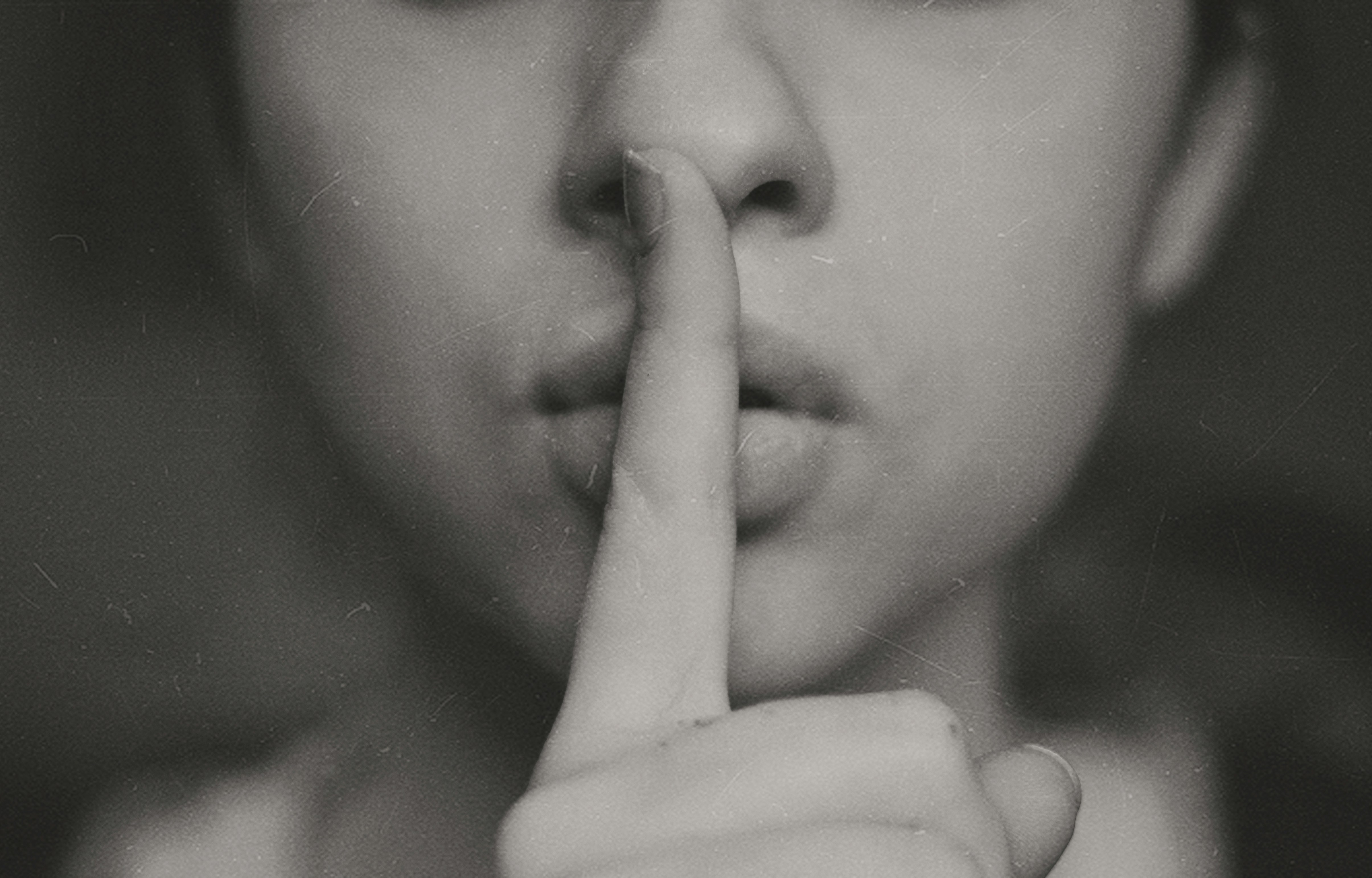 Black and white image - female with one finger over mouth as if silencing her 