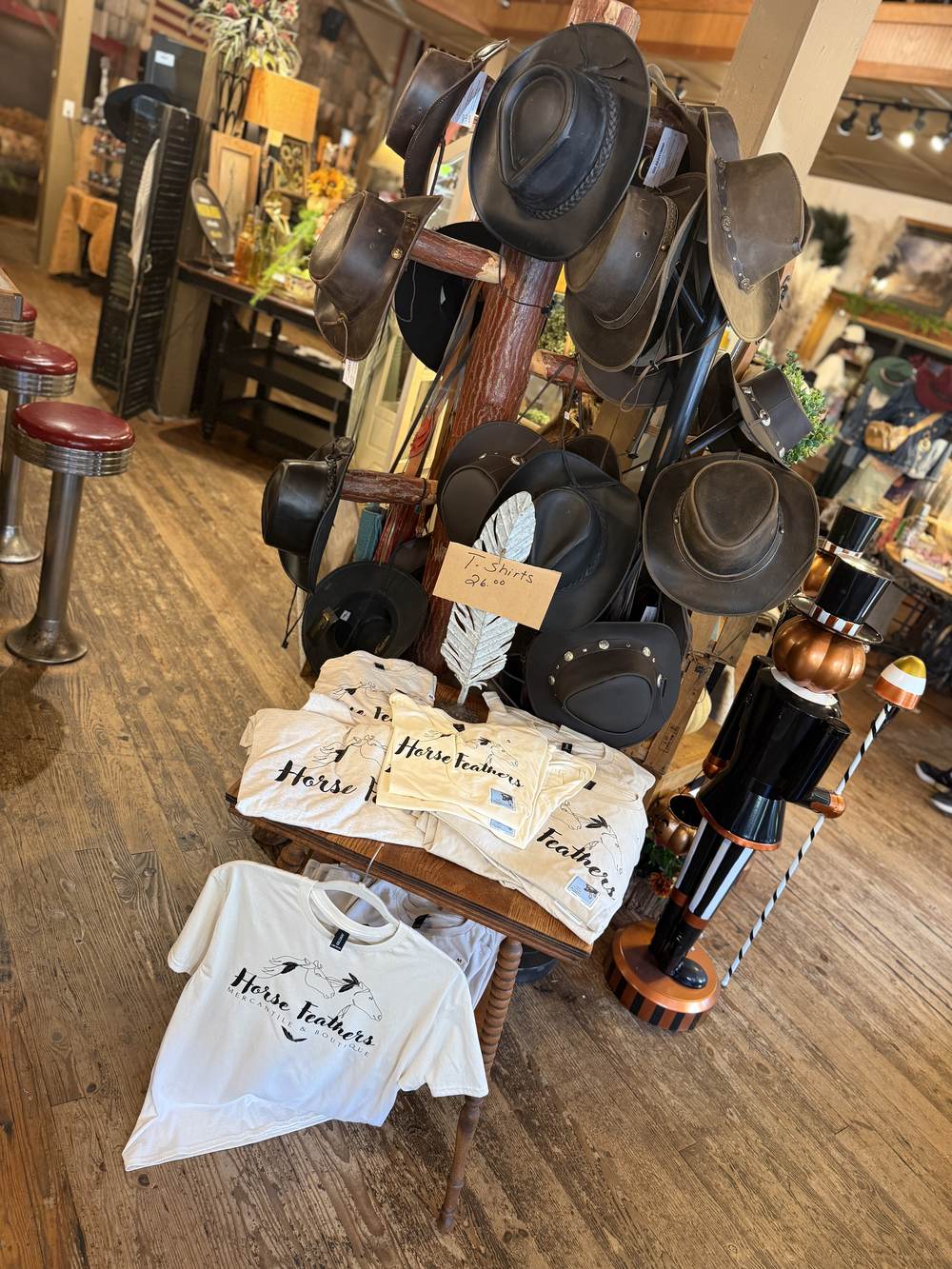 Leather and felt hats on a wooden hat tree beside folded Horse Feathers t-shirts