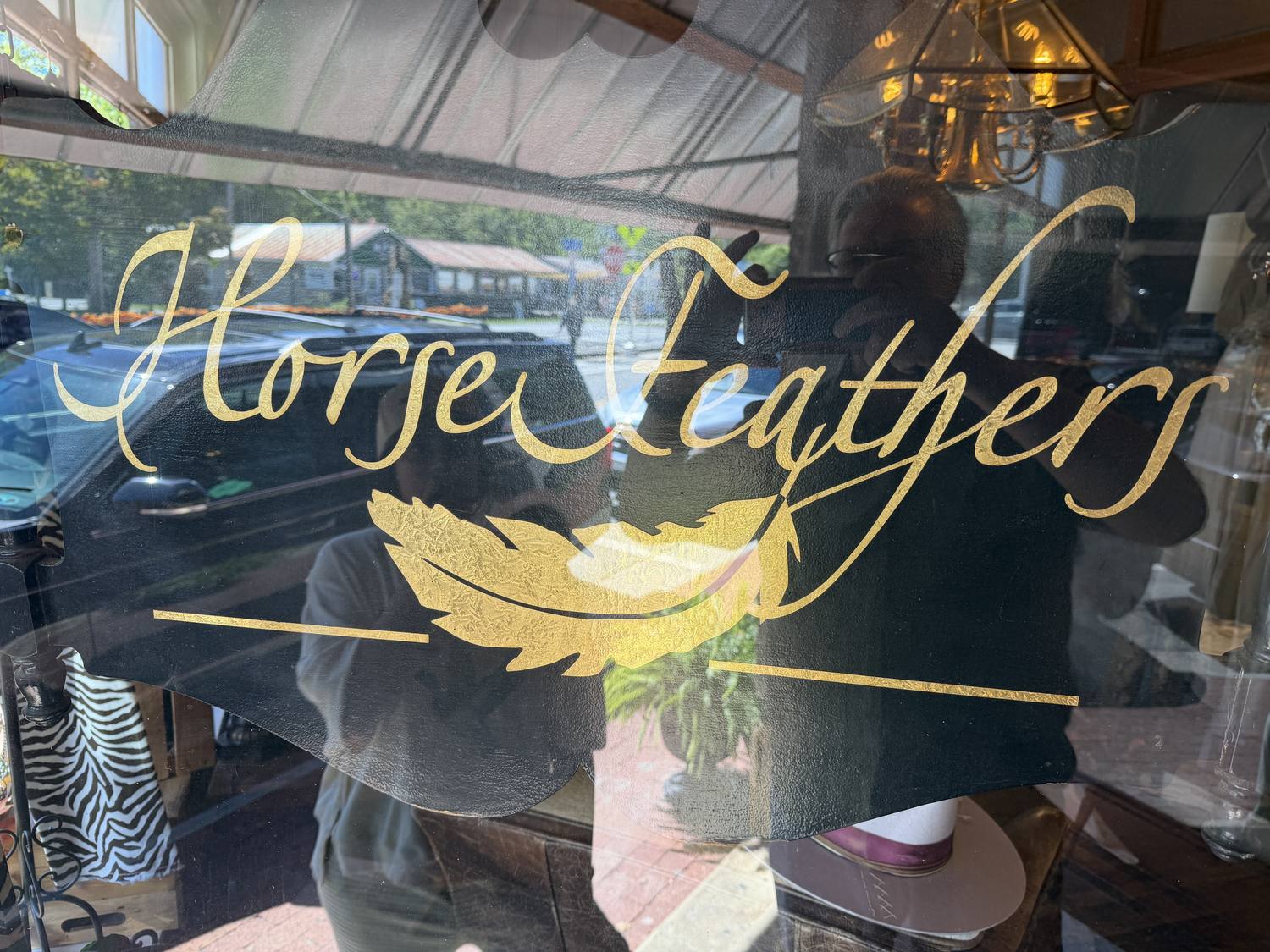 The gold Horse Feathers script and feather painted on the front window on Front Street in Dillsboro