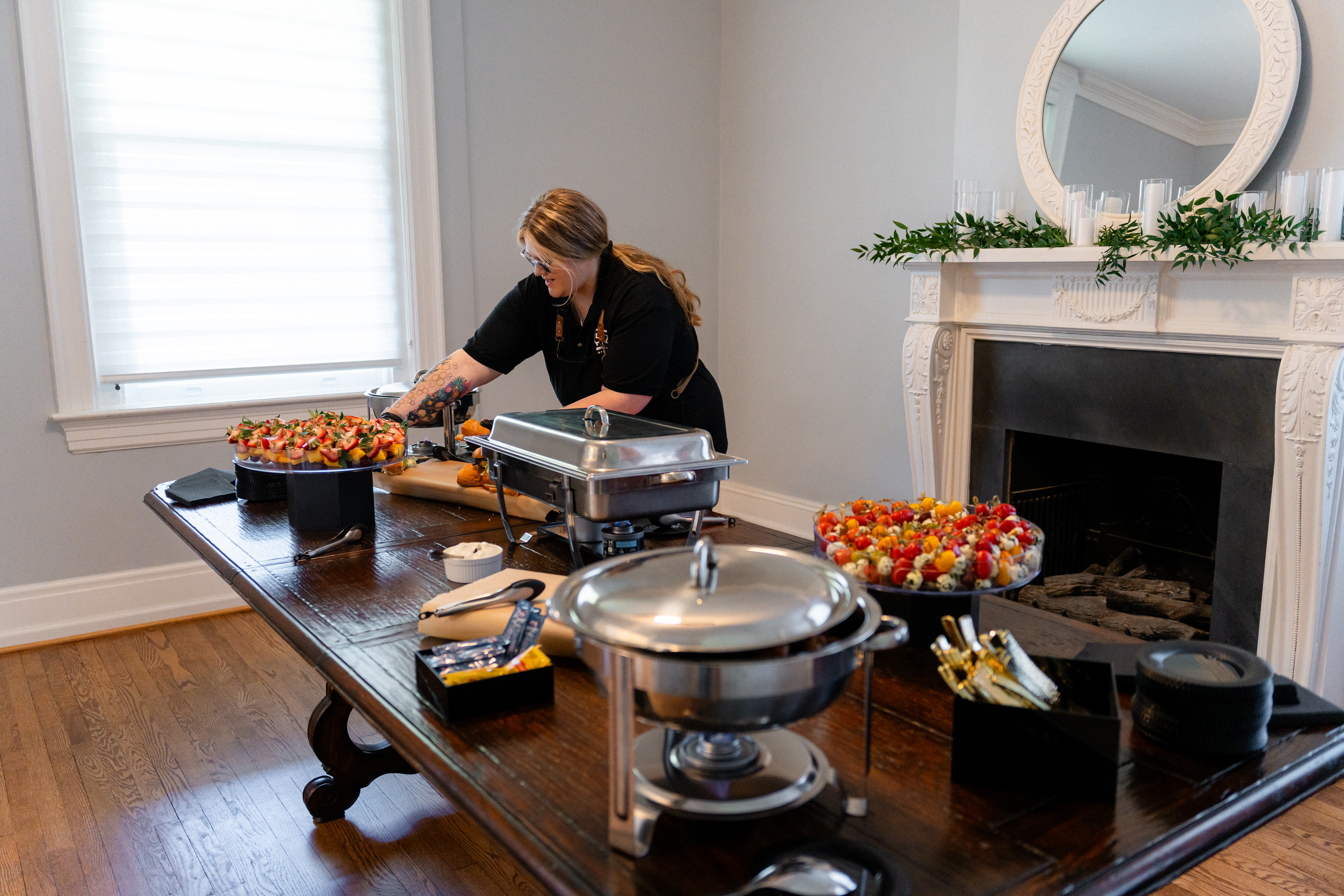 Catering staff member preparing appetizers and chafing dishes beside a decorated fireplace at Bent Oaks Manor