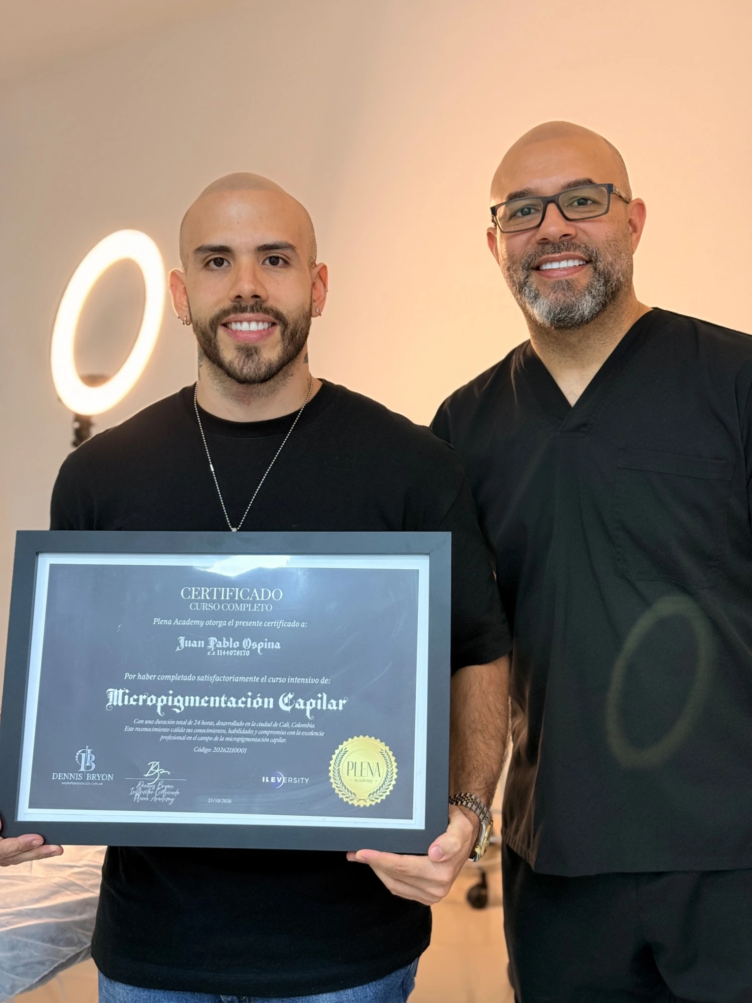 Estudiante junto a Dennis Bryon con su certificado de micropigmentación capilar.