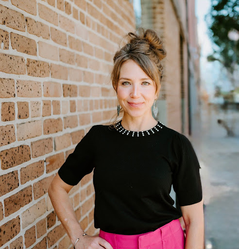 Meg Lamm, Licensed Massage Therapist and business mentor, smiling confidently against a brick wall background