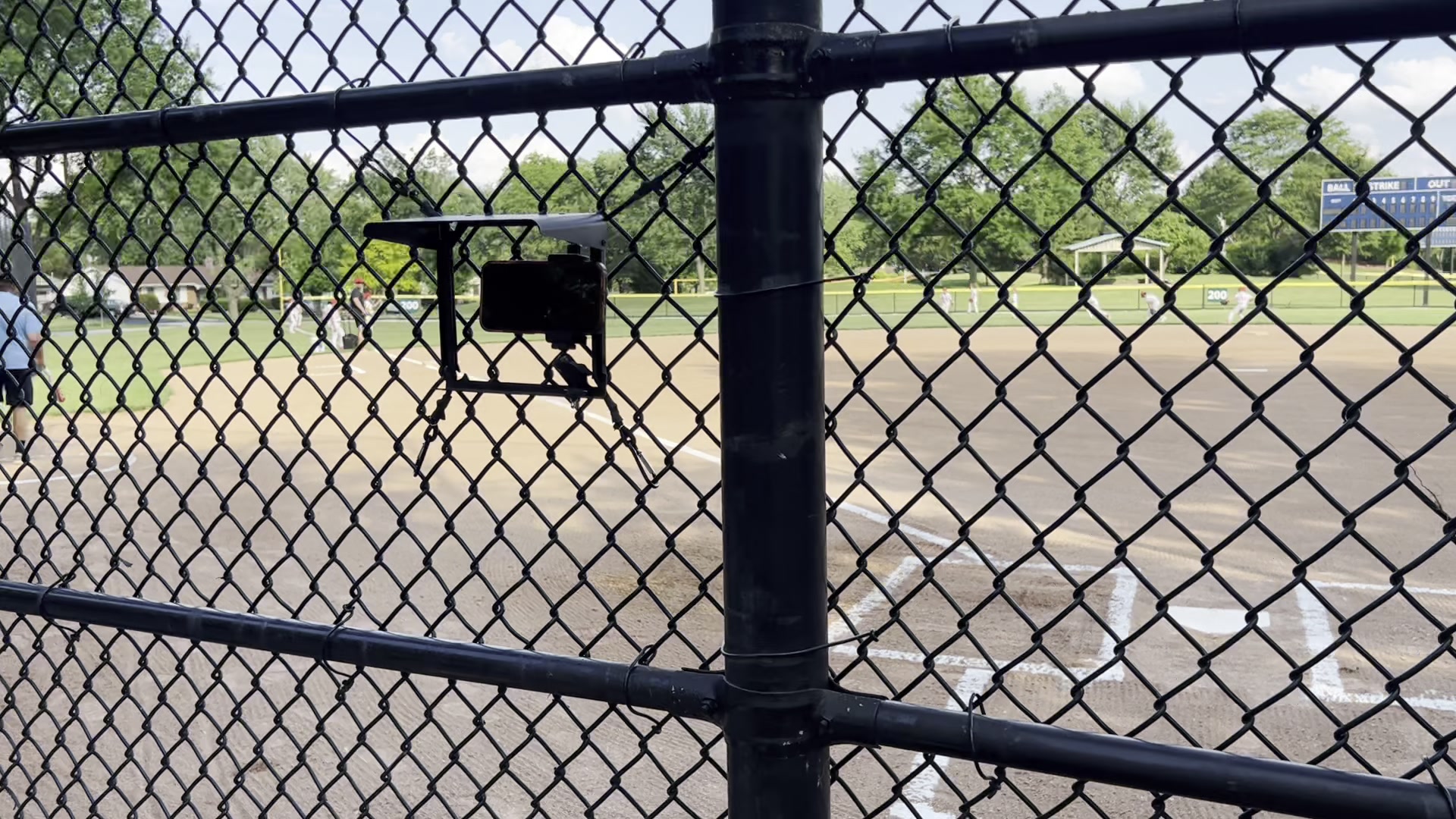 Phone mounted on a tripod behind a chain-link backstop, pointed at the field.