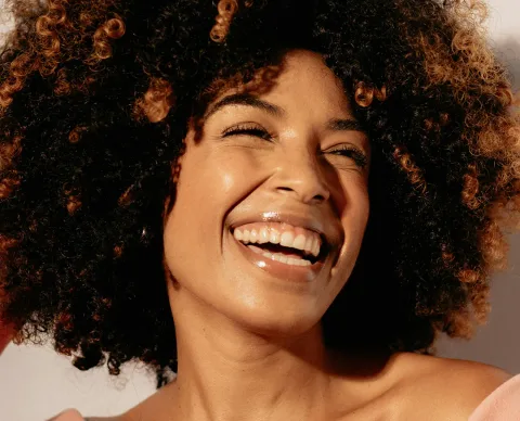 A smiling client with luminous, healthy skin in warm sunlight