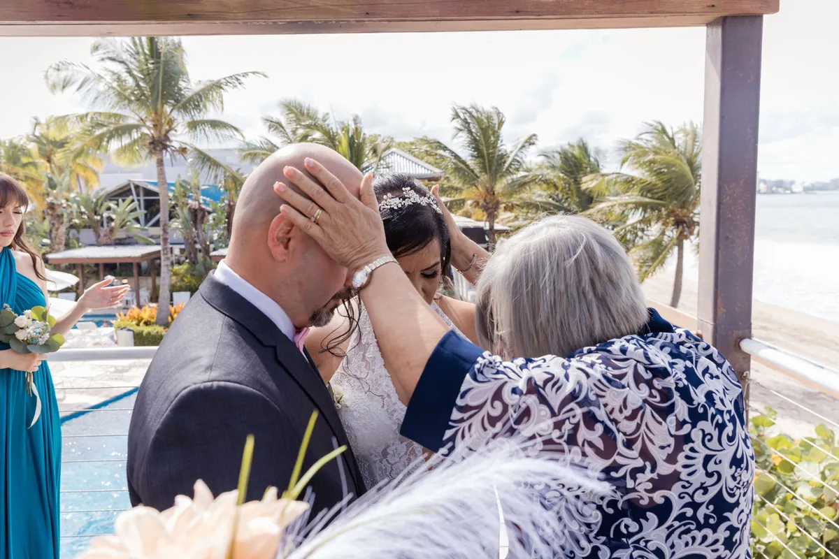 Una señora bendice al novio con la mano en su cabeza durante la ceremonia junto a palmas