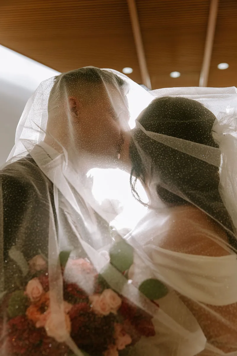 Beso de la pareja bajo el velo con luz cálida a contraluz