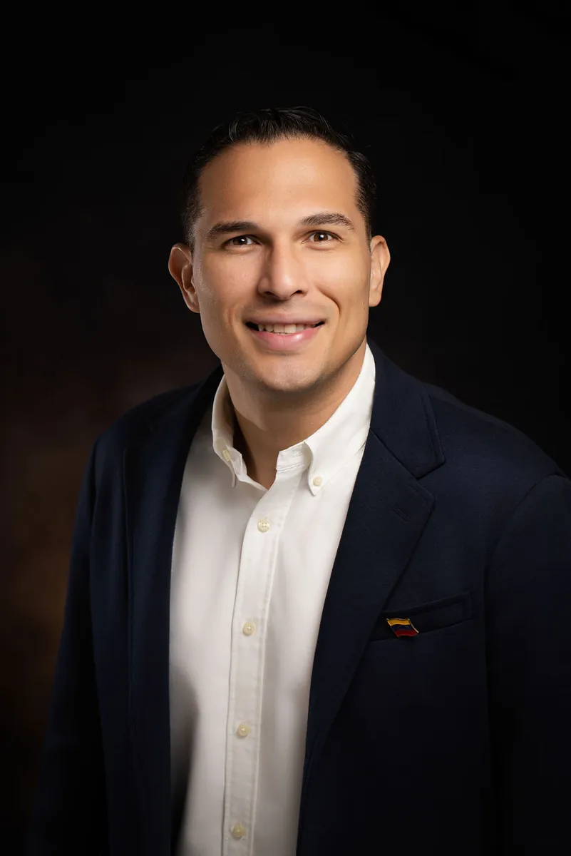 Retrato profesional de un hombre sonriente con blazer azul marino y camisa blanca sobre fondo marrón de estudio