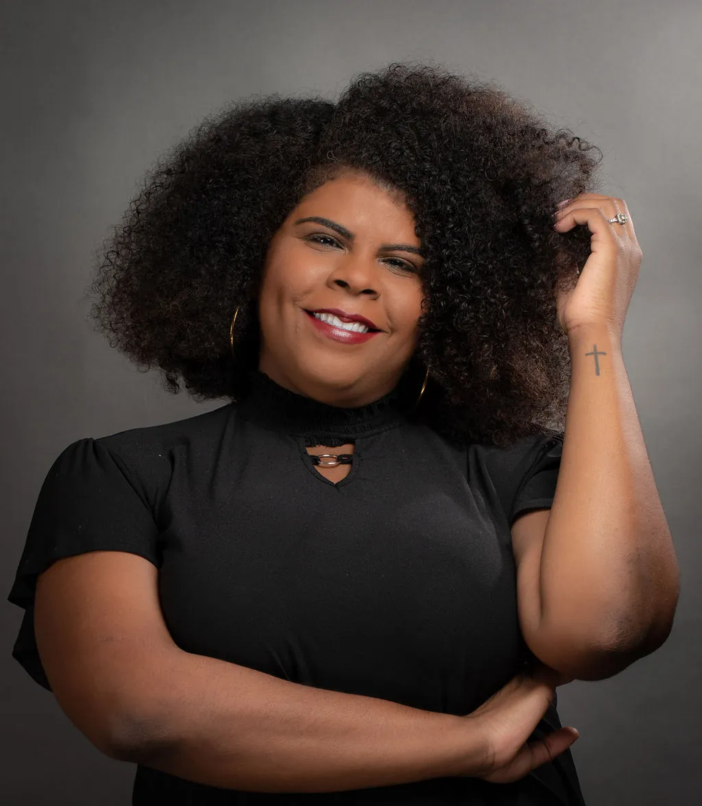 Retrato de estudio de una mujer afrodescendiente con cabello afro natural y blusa negra sonriendo sobre fondo gris