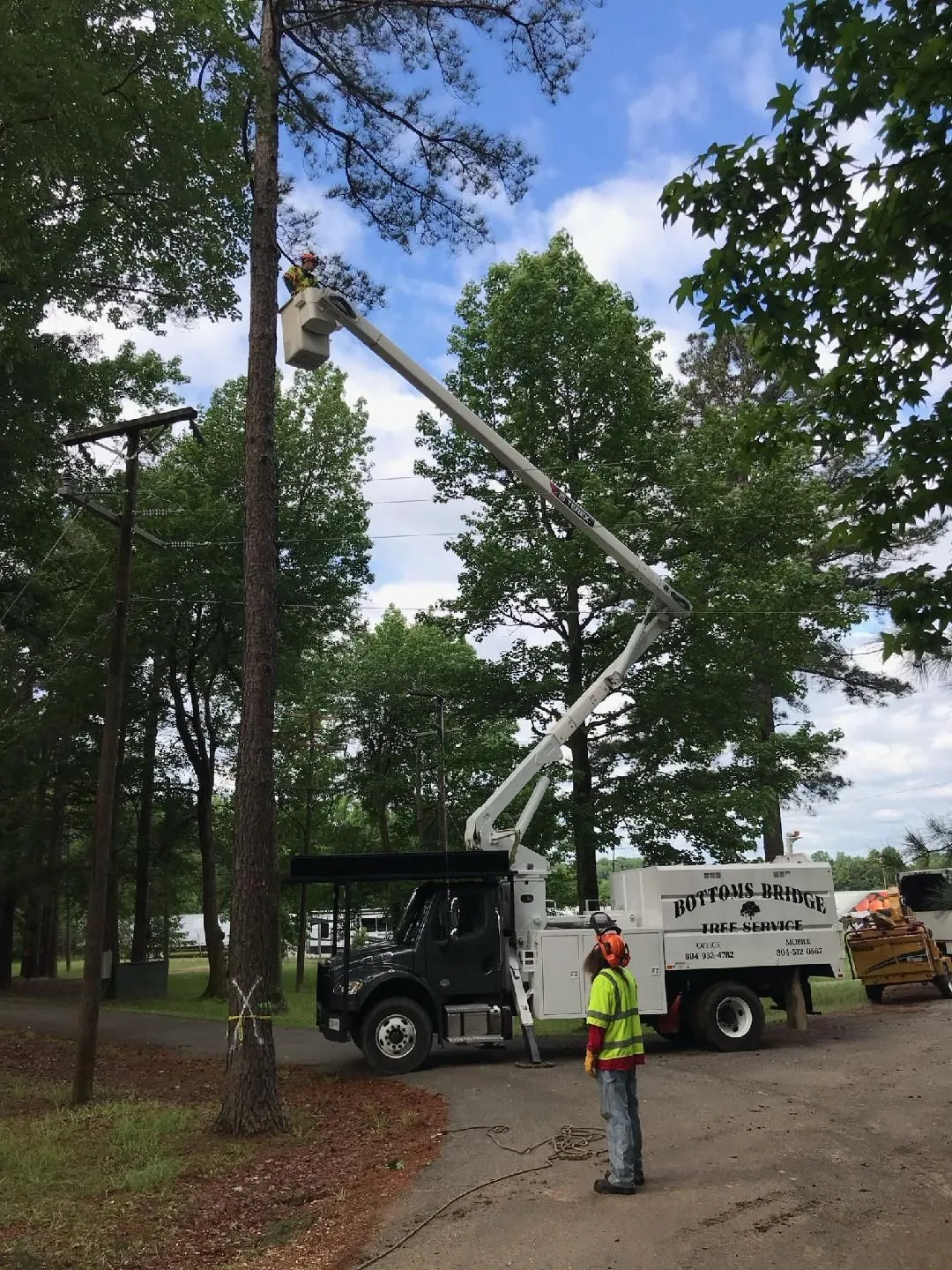 High-reach boom lift clearing overhanging limbs over roofline